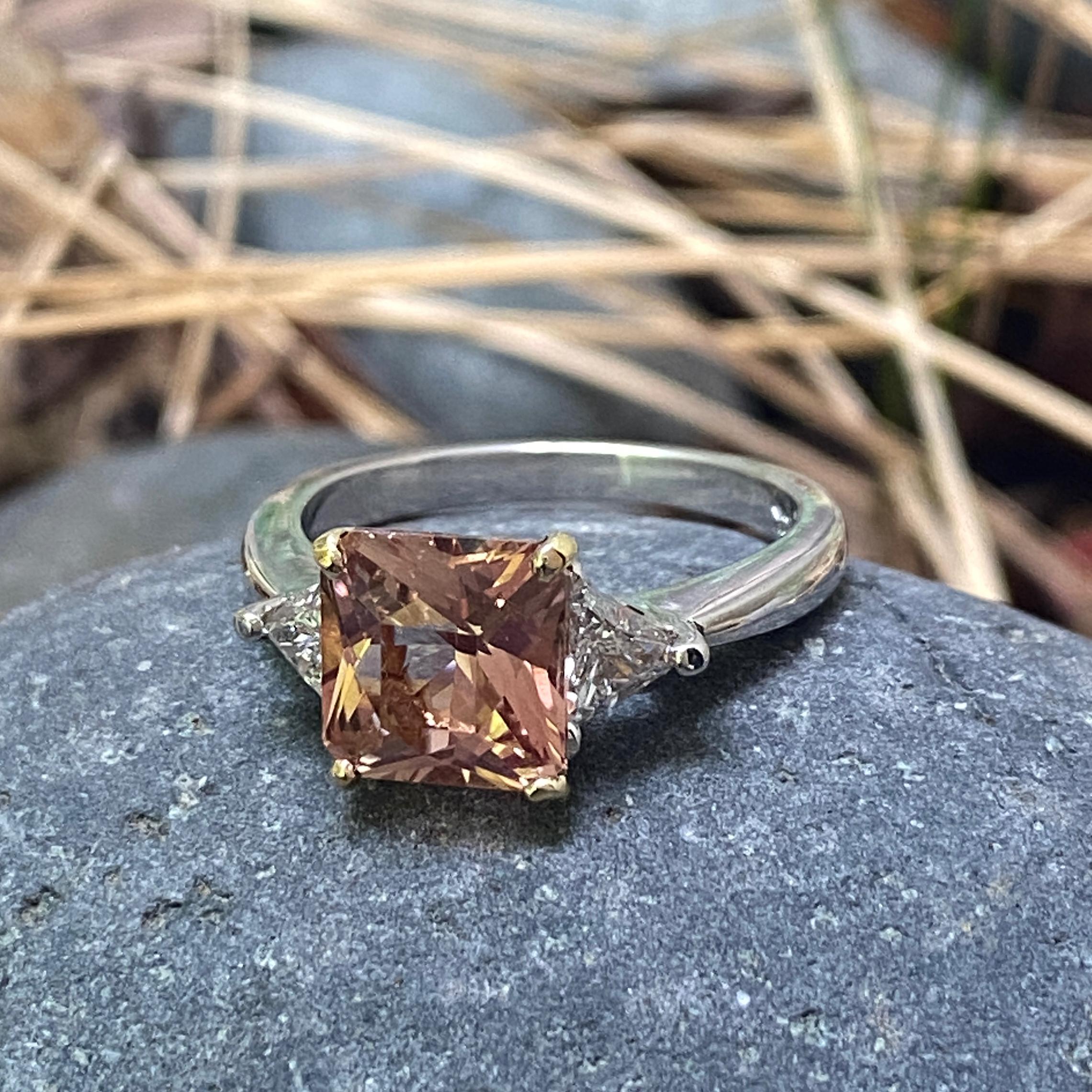 Two clean and bright, hard-to-find straight trillions gird a mixed cut Oregon Sunstone in this sleek platinum ring.  

This ring was originally set with a yellow diamond, so the center prong basket is deep yellow 18 karat yellow gold instead of