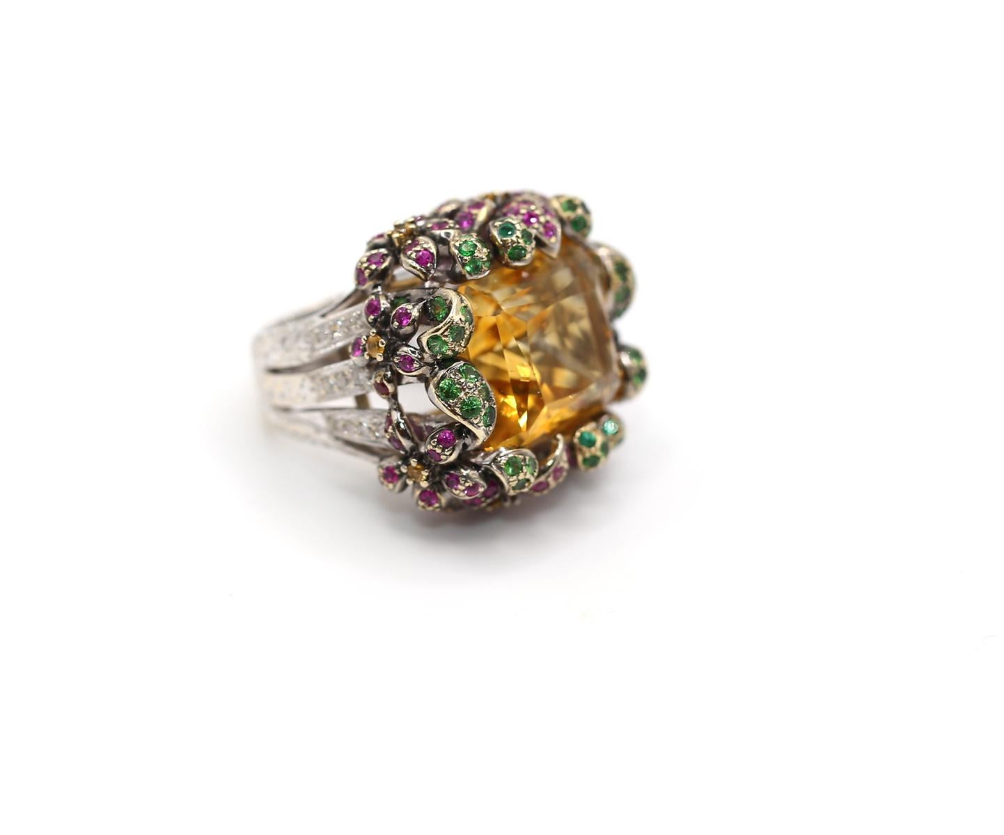 22 Ct Citrine Tsavorite Diamants Ruby Floral Cluster Ring in 18K Gold.
Cette bague de cocktail sculpturale et spectaculaire est ornée d'une belle citrine jaune-cognac, d'une riche saturation et d'un magnifique feu interne. La citrine est taillée