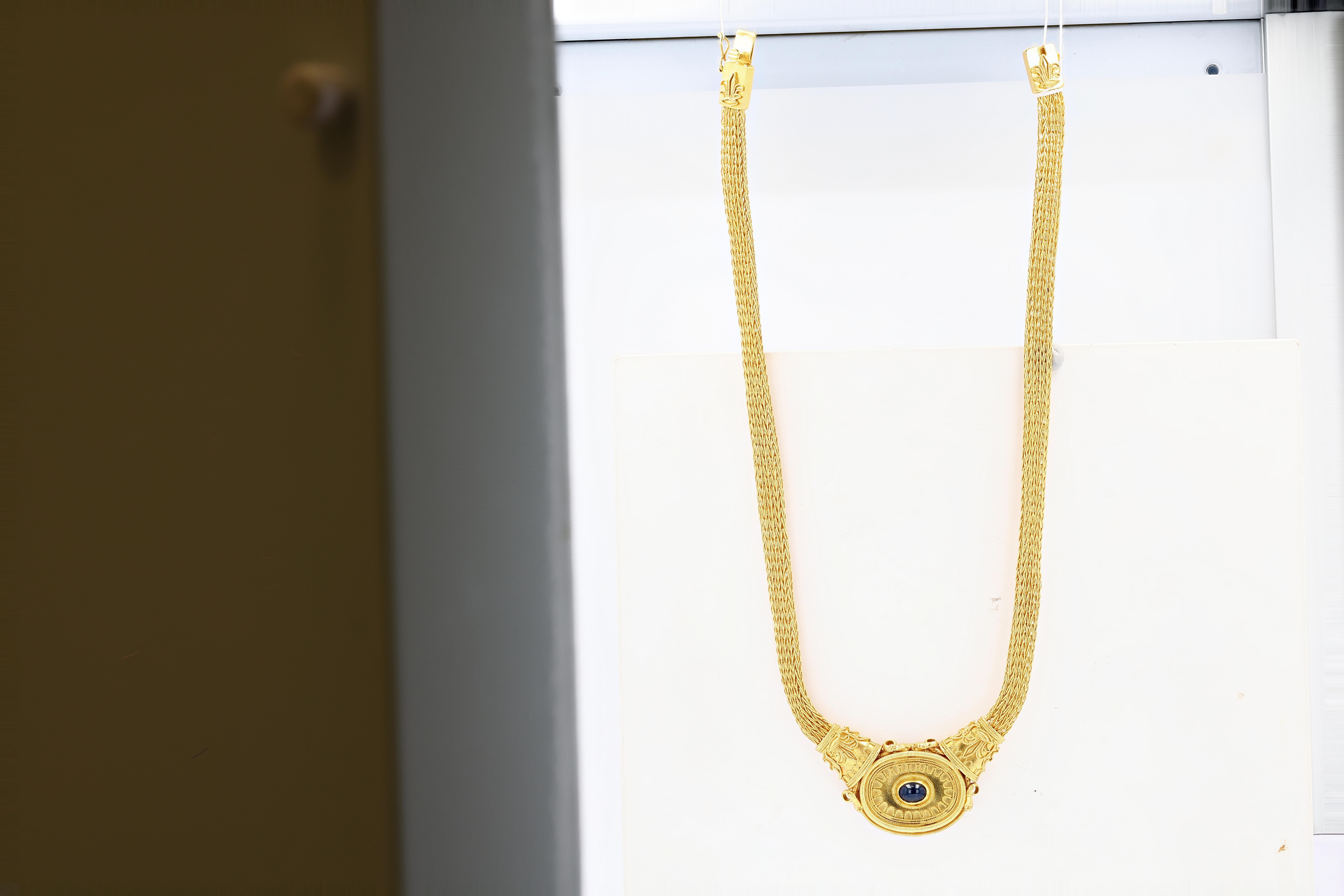 A highly unusual and rare 22 karat yellow gold integrated pendant necklace prominently featuring a large dark blue cabochon stone in a bezel setting. The pendant is extremely detailed, featuring fine jewelry making techniques throughout; leaf motifs