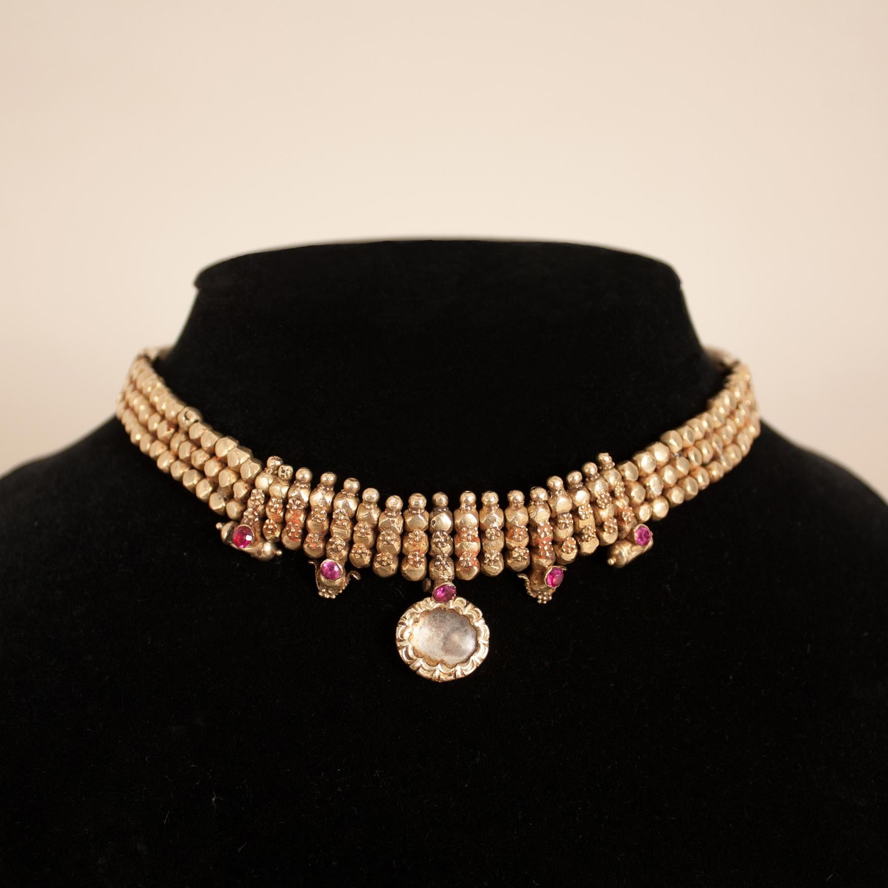 A 22 karat gold over wax bead traditional choker from Rajasthan, India, circa 1930. This exquisite necklace is adorned with fine gold granulation, faceted rubies, a foil-backed crystal centerpiece, two delicate amulets, and two ornaments. The