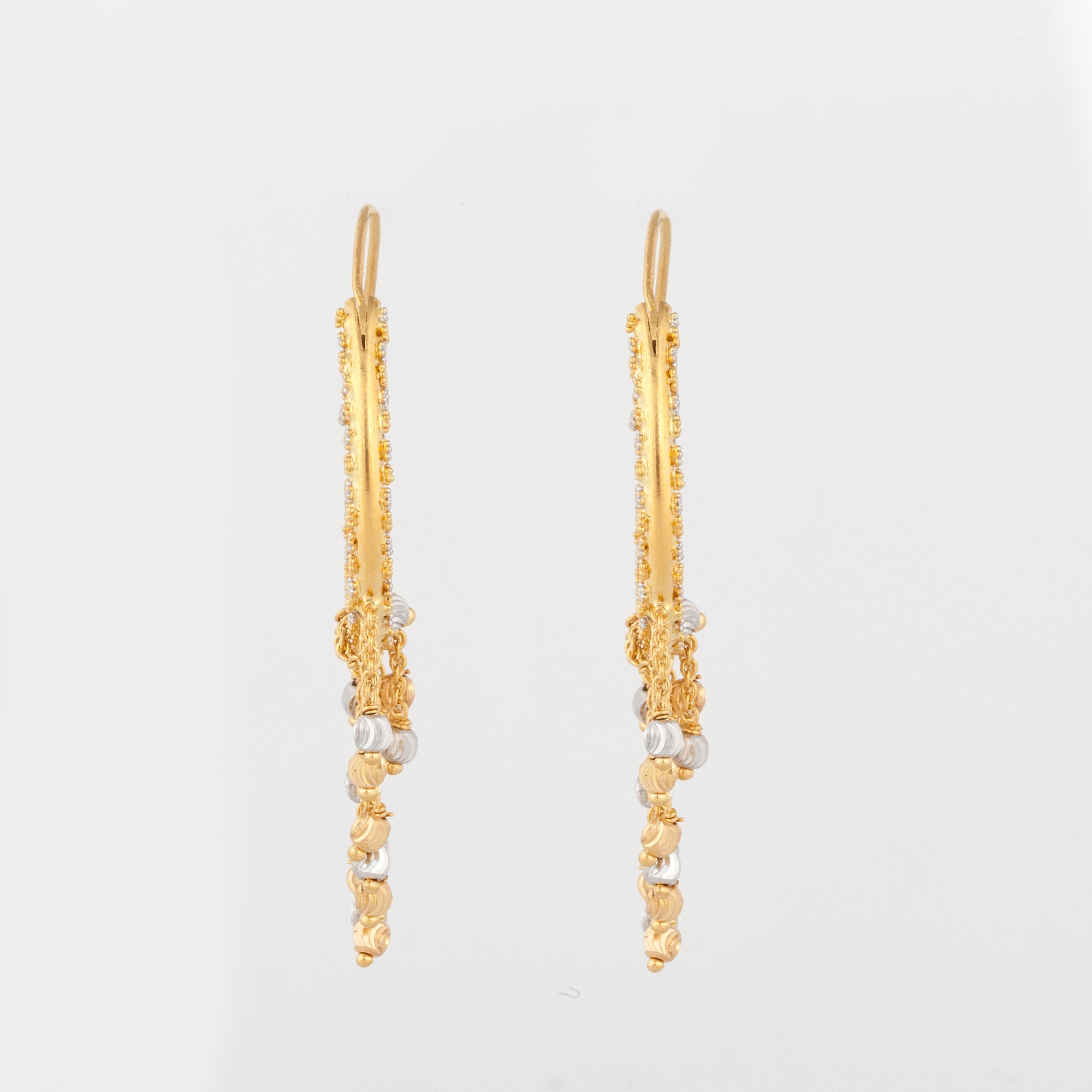 Hoop earrings which are crafted in yellow and white 22K gold.  There are chains dangling from the bottom with small balls attached at the end of each chain.  Etruscan work along each outside edge.  Measure 2-1/8
