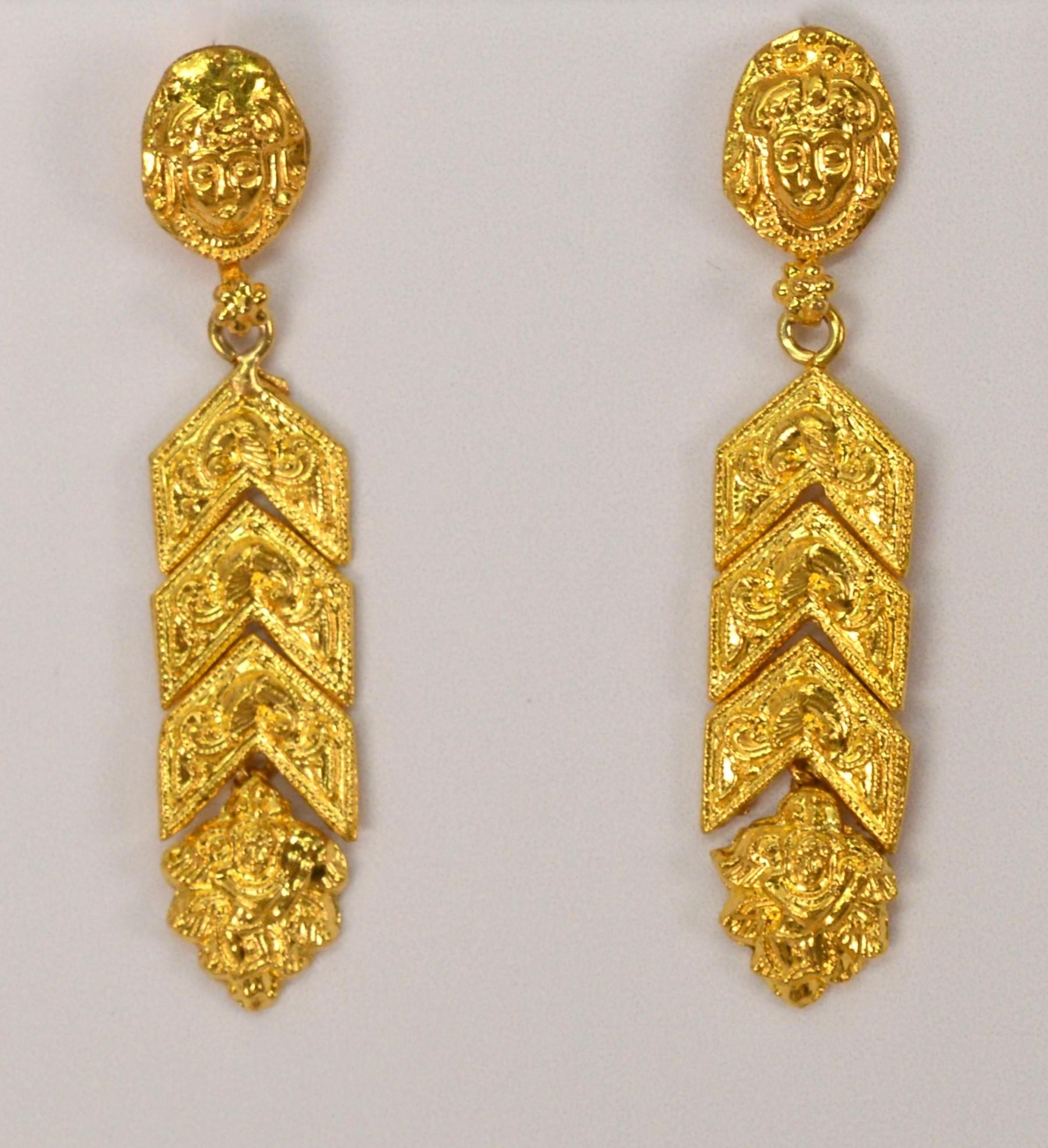 Hand crafted in rich 22 karat yellow gold, these ribbon inspired drop earrings show beautifully and can dress up any look with it bold gold color. The pair starts with its stud displaying a mythical figure head followed by a ornately decorated