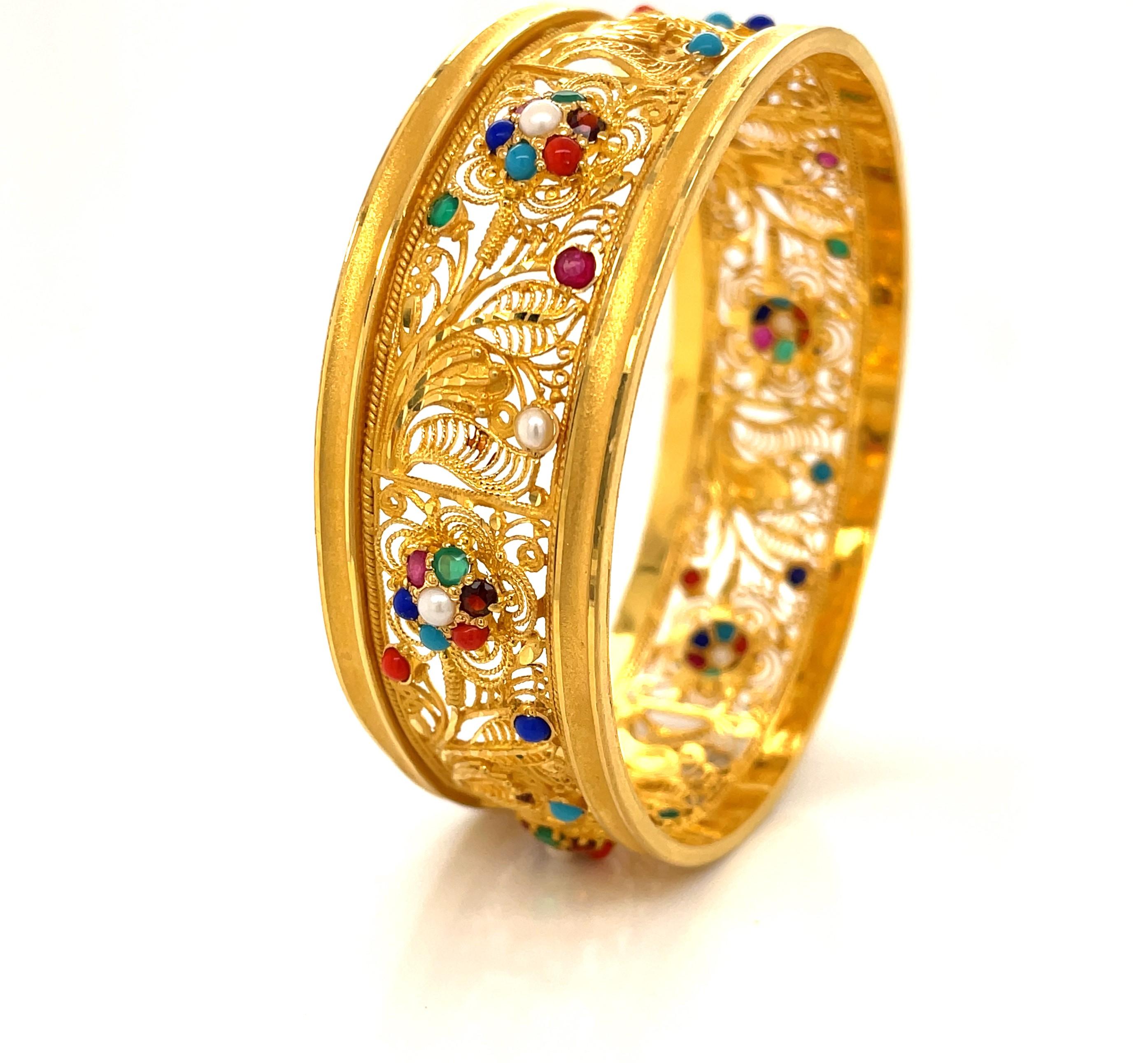 Truly impressive, this unique bangle bracelet is expertly handcrafted with floral and vine filigree in textures of satin and bright twenty two karat 22K yellow gold.  The intricate gold flora is further enhanced with various colorful gemstone