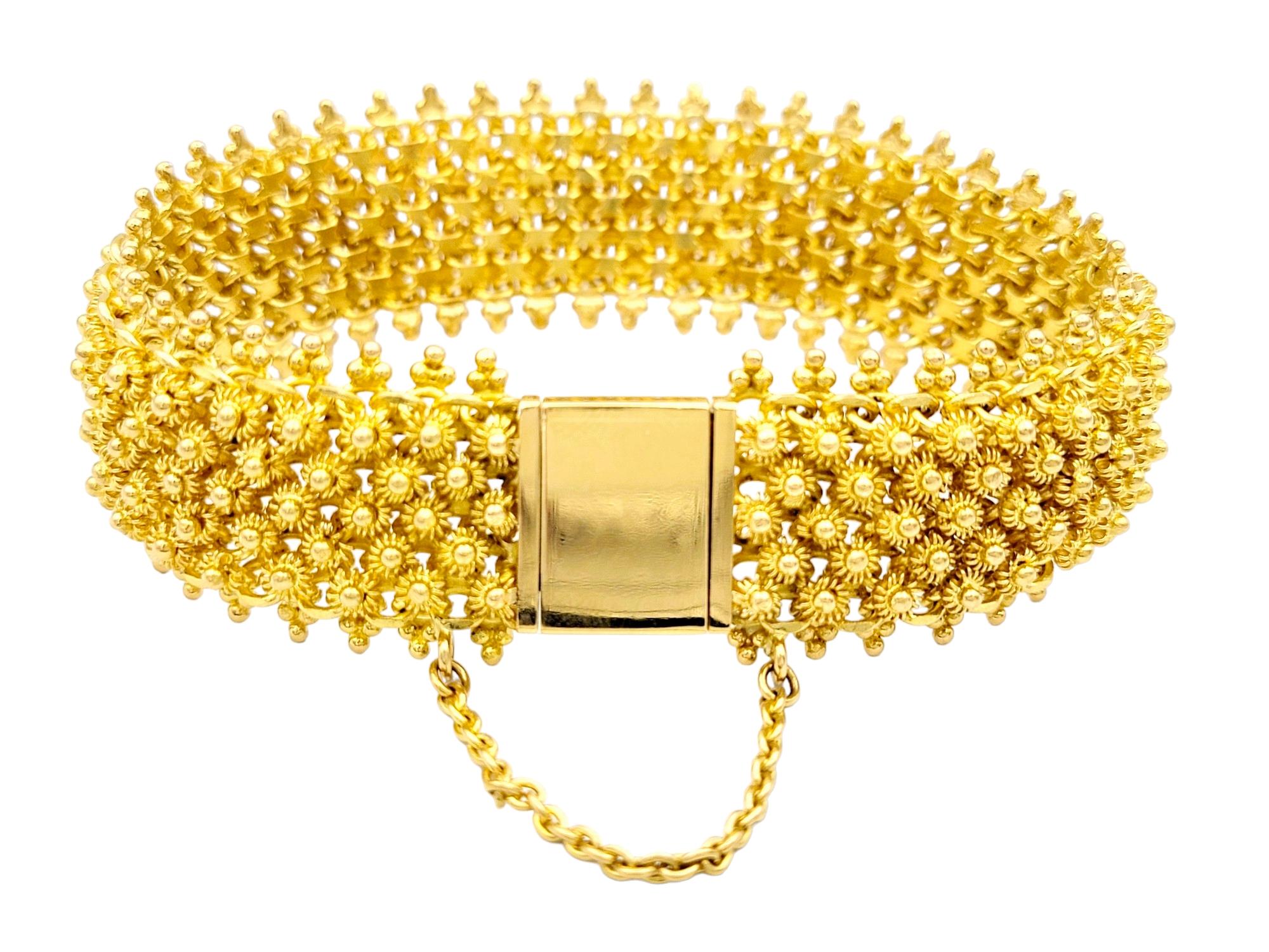 This luxurious textured gold bracelet is crafted in opulent 22 karat yellow gold. The bracelet boasts a wide and flexible design, composed of a series of intricate wire flower motifs that weave together seamlessly, creating a unique and luxurious