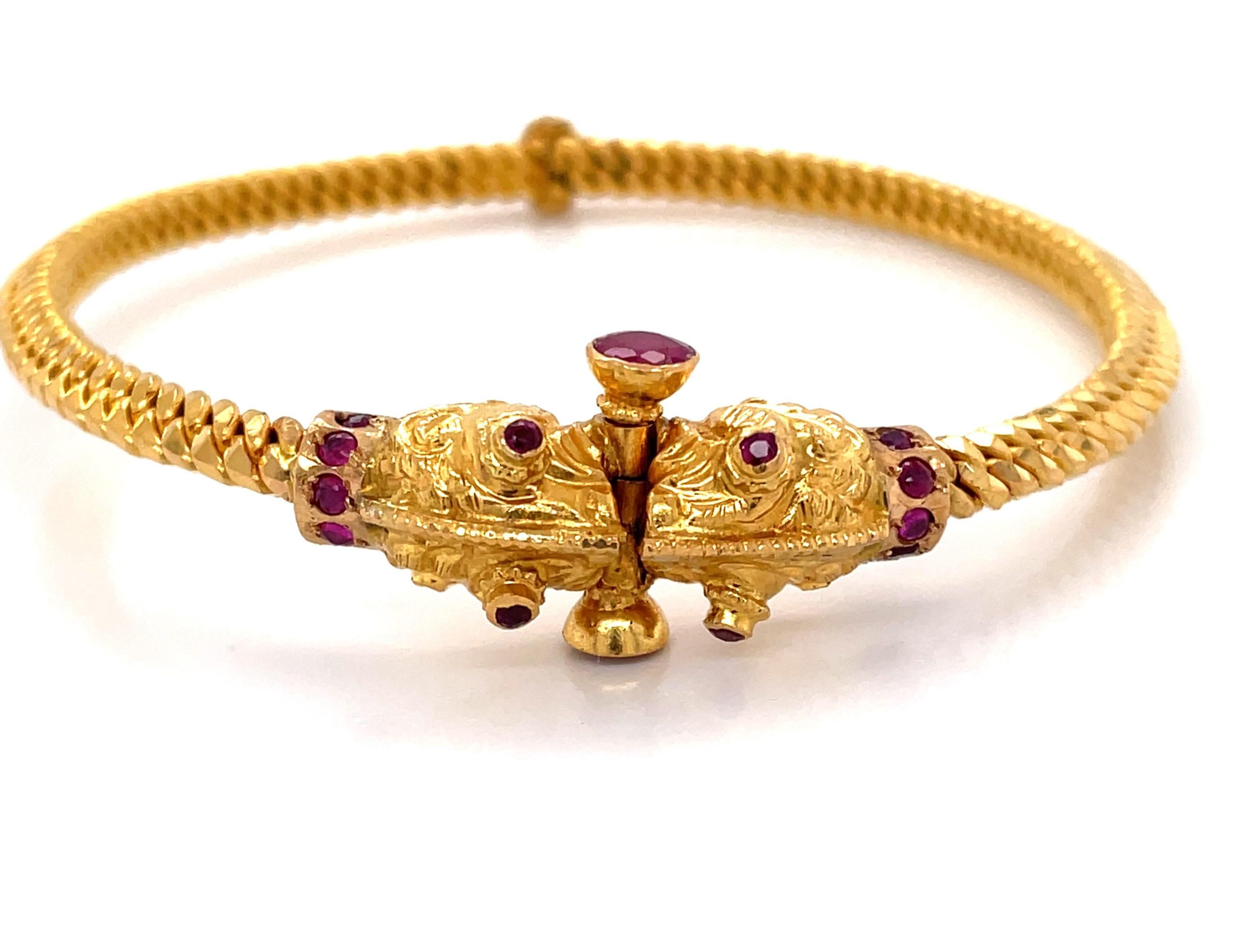Unusual and artisan-made, this twenty two karat (22K) yellow gold bangle bracelet is alluring with mystical serpent heads that meet and are adorned with .54 carats of hand cut  natural rubies. Crafted with intricate screw closure, this artful 2-1/2