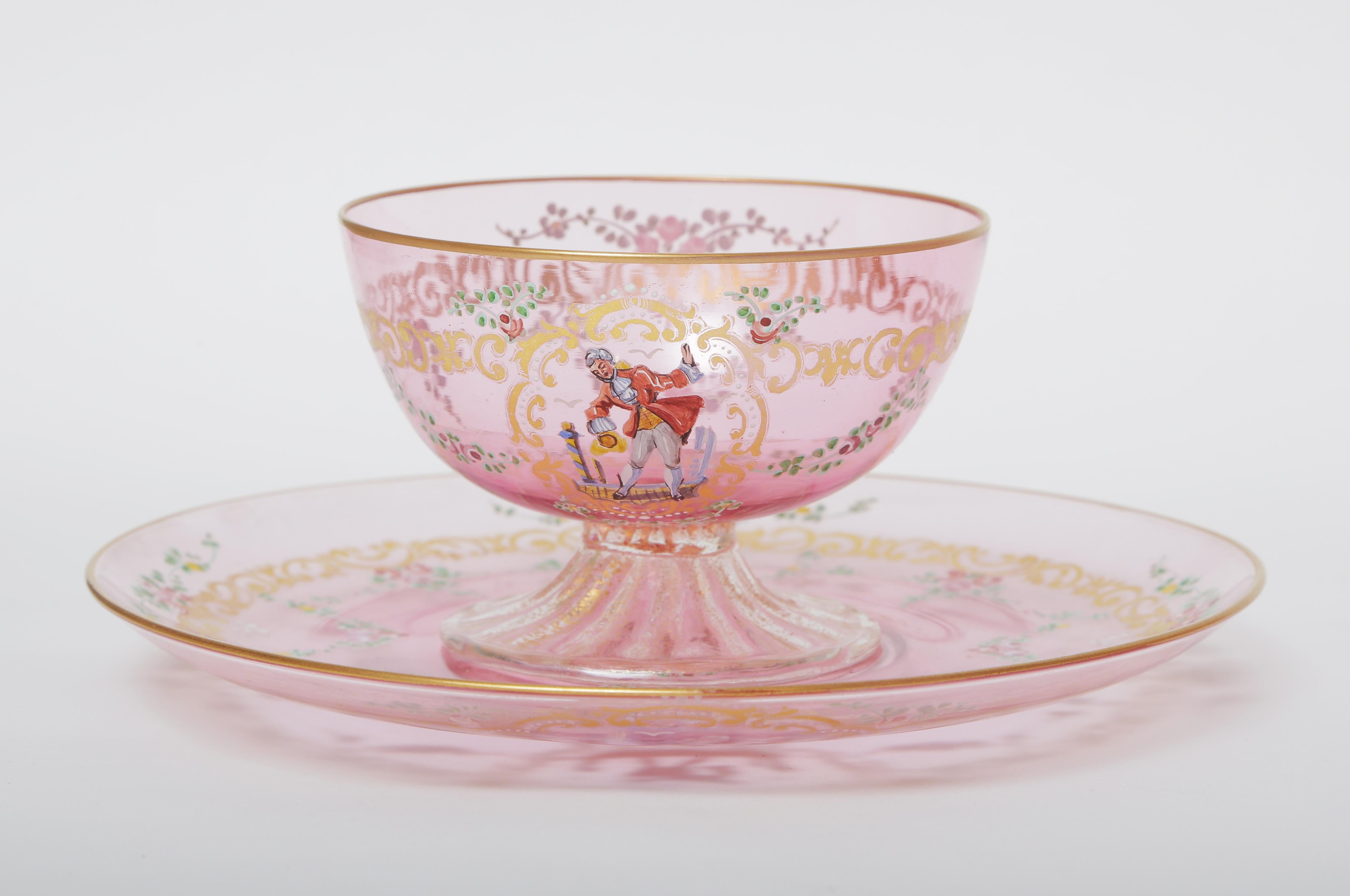 An exquisite set of 11 dessert coupes and 11 matching dessert under plates in a pretty pink color. These lovely pieces feature hand enameled figural and floral details with a gilt foliate swag. We love the shape of the bowl and how nicely it sits on