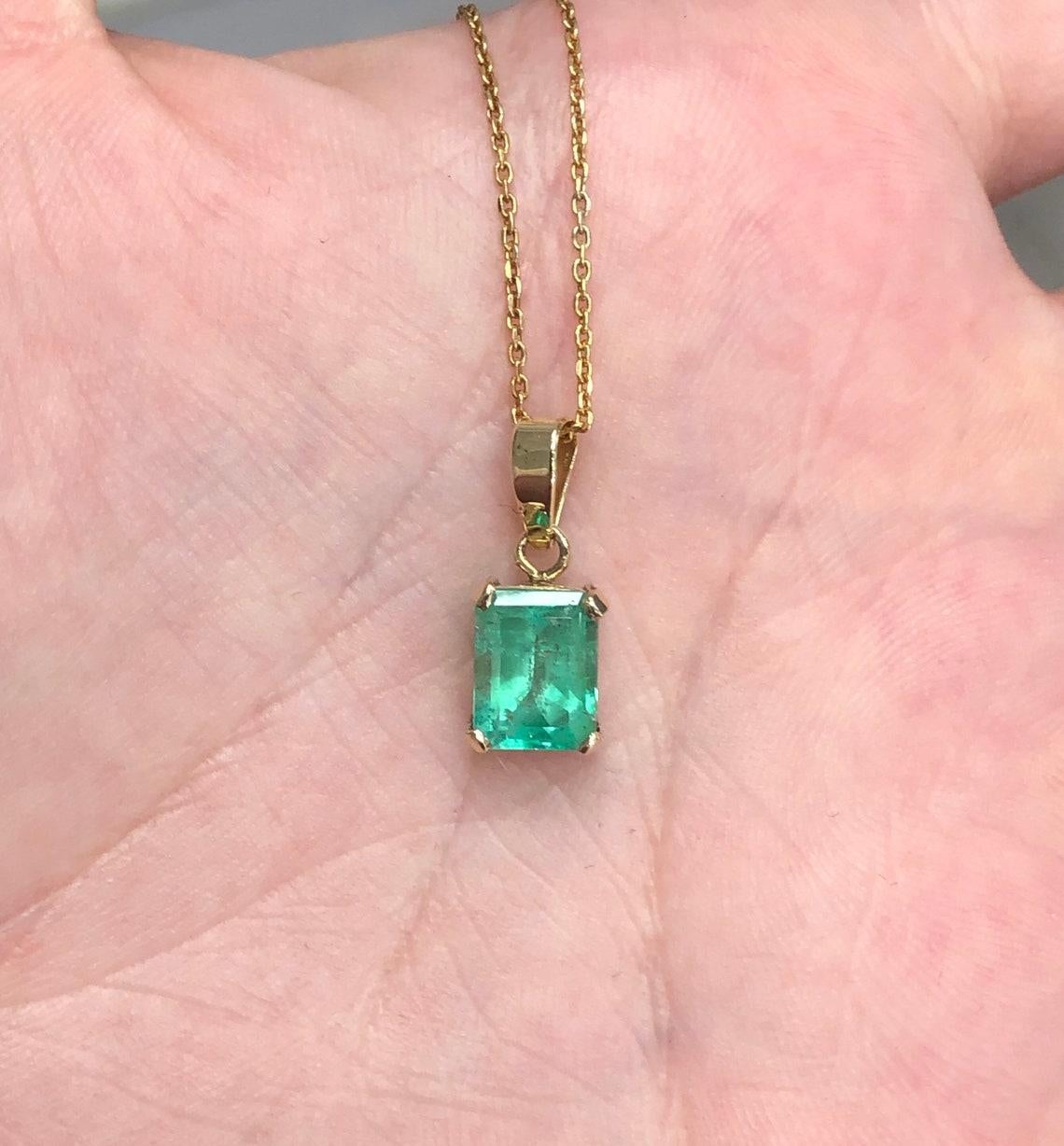Featured here is a stunning emerald cut Colombian emerald necklace in fine 14K yellow gold. Displayed in the center is a medium-green emerald with very good clarity, accented by a simple four-prong gold mount, allowing for the emerald to be shown in