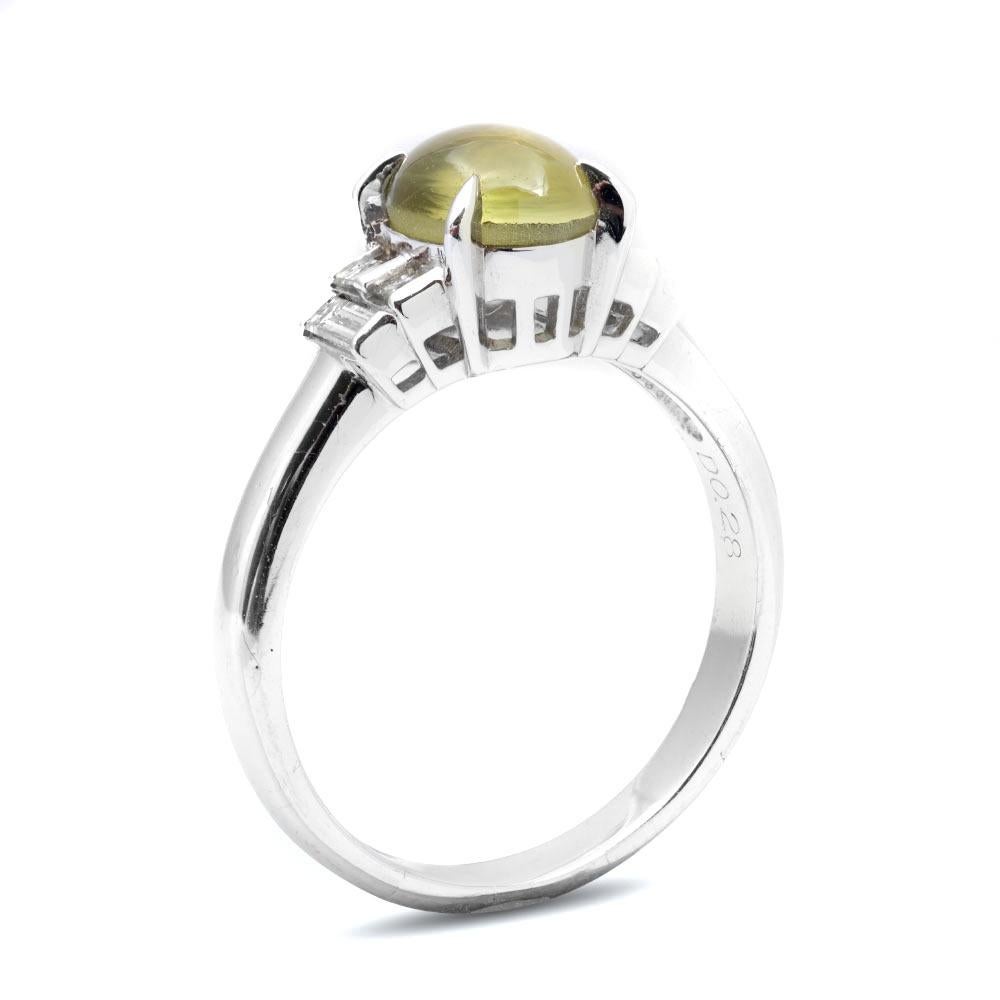 The silvery notes of this platinum ring give it a contemporary feel that pairs well with the symmetrical design of the accentuating diamonds. Set with the greenish yellow Cats Eye Chrysoberyl that displays an elegant milk and honey effect it