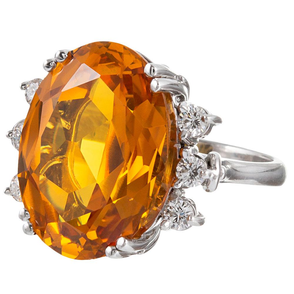 An eye-catching 22.03 carat oval faceted citrine sit nestled in split prongs and flanked by a trio of round white diamonds in its 18 karat white gold mounting. The color of the major stone is complimentary to all palettes, its neutral hue offering a