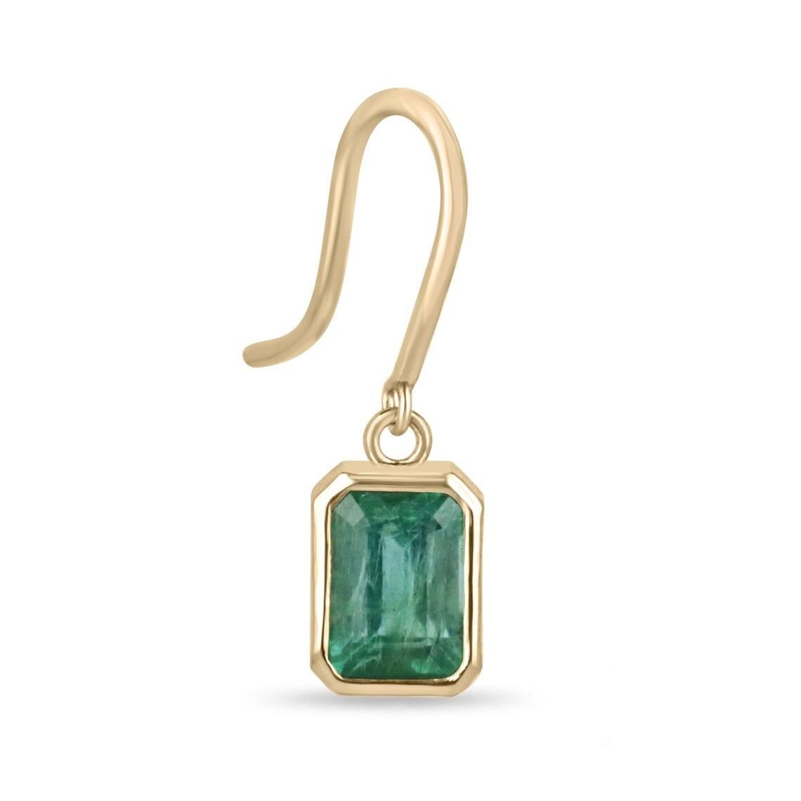 These emerald dangle earrings showcase two emerald cut emeralds with a combined weight of 2.20 carats. The emeralds exhibit a lovely dark lush green color with unique clarity and luster. They are elegantly bezel-set, providing a secure and sleek