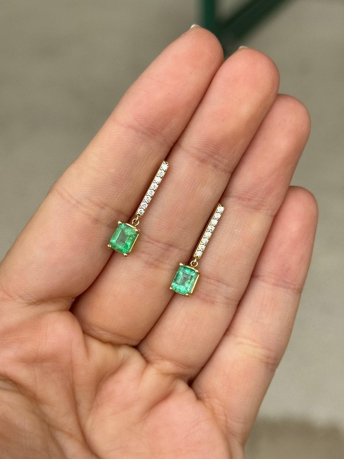 Elevate your style with our stunning emerald and diamond bar dangle earrings, boasting a total combined carat weight of 1.90 carats of natural emeralds. Set in four prongs for secure elegance, these lustrous medium-green emeralds cascade gracefully