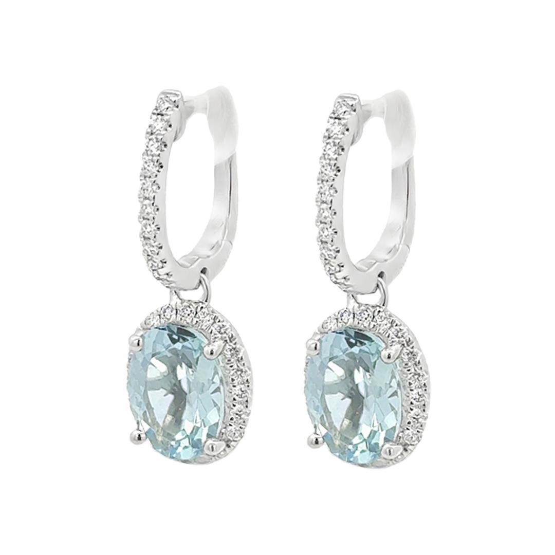 A stylish pair of dangle earrings, featuring oval cut aquamarines weighing 2.21 carats total, set on four rounded prongs. Surrounded by a halo of round cut diamonds and accented by a diamond encrusted upper dangle. Diamonds weigh 0.32 carat total.