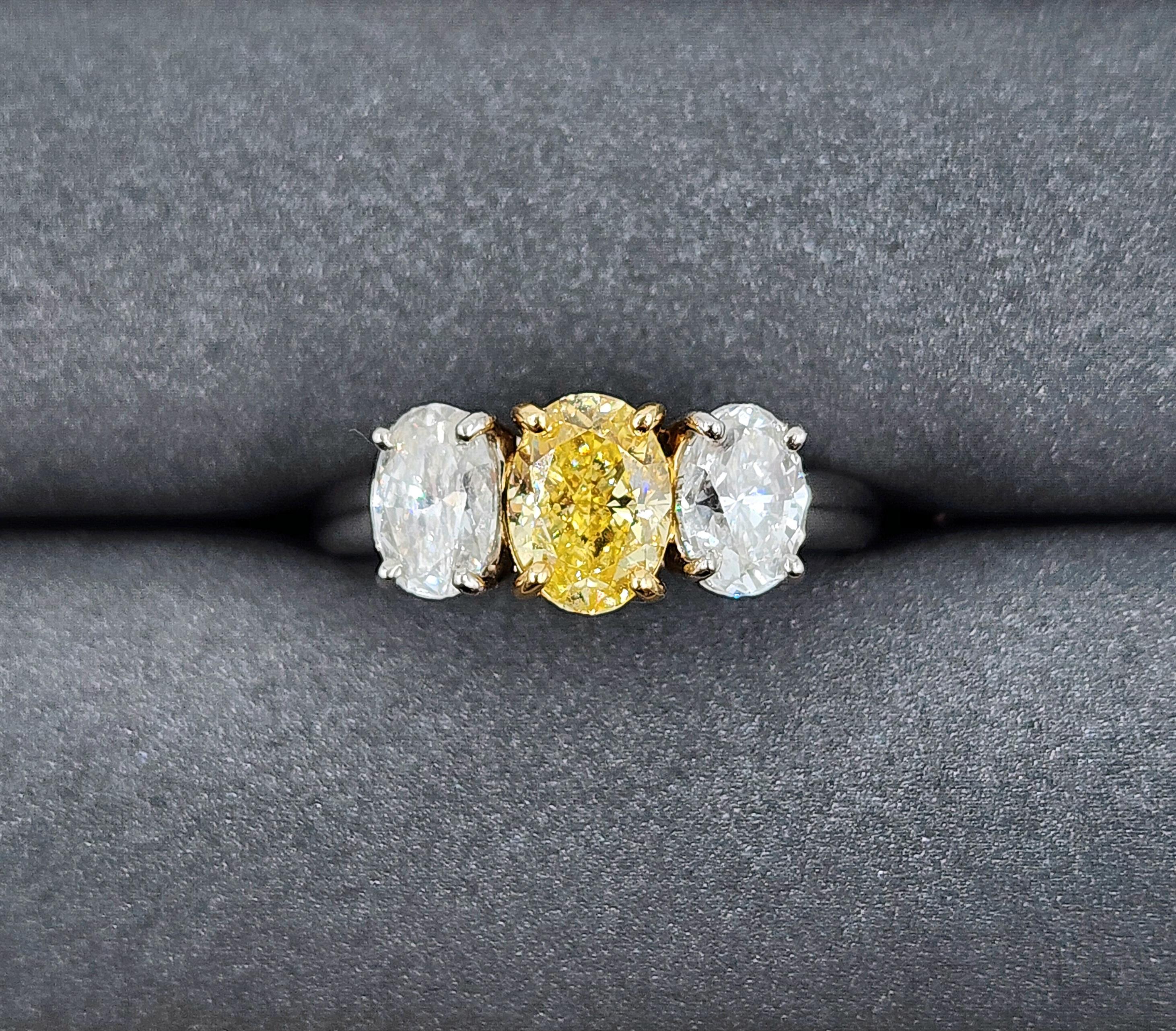 Questo splendido anello con tre pietre di diamante giallo e bianco da 2,21 carati è l'aggiunta perfetta a qualsiasi collezione di gioielli. La pietra centrale è un bellissimo diamante giallo naturale del peso di .96 Fancy giallo intenso accompagnato