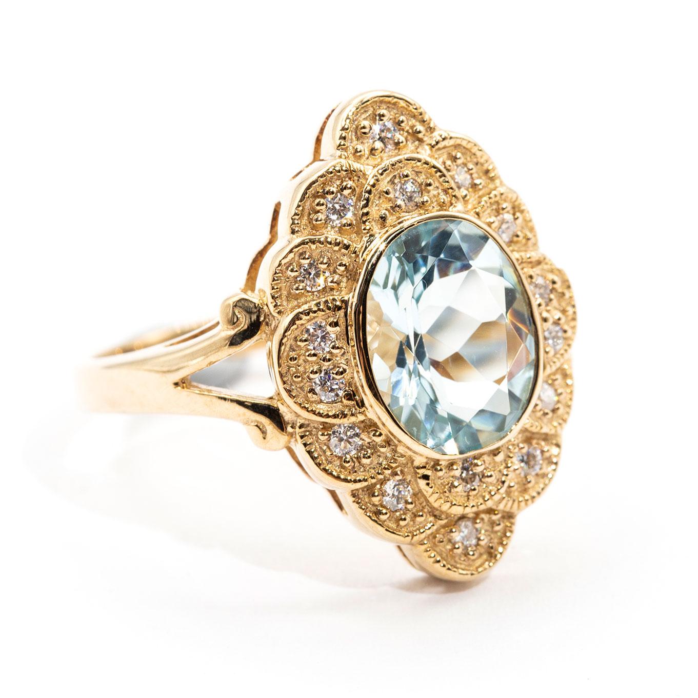 Crafted in 9 carat yellow gold is this breathtaking vintage inspired ring that boasts a striking oval cut 2.22 carat bright light blue Aquamarine encompassed by a gorgeous scalloped border of carefully set round brilliant cut diamonds. We have named