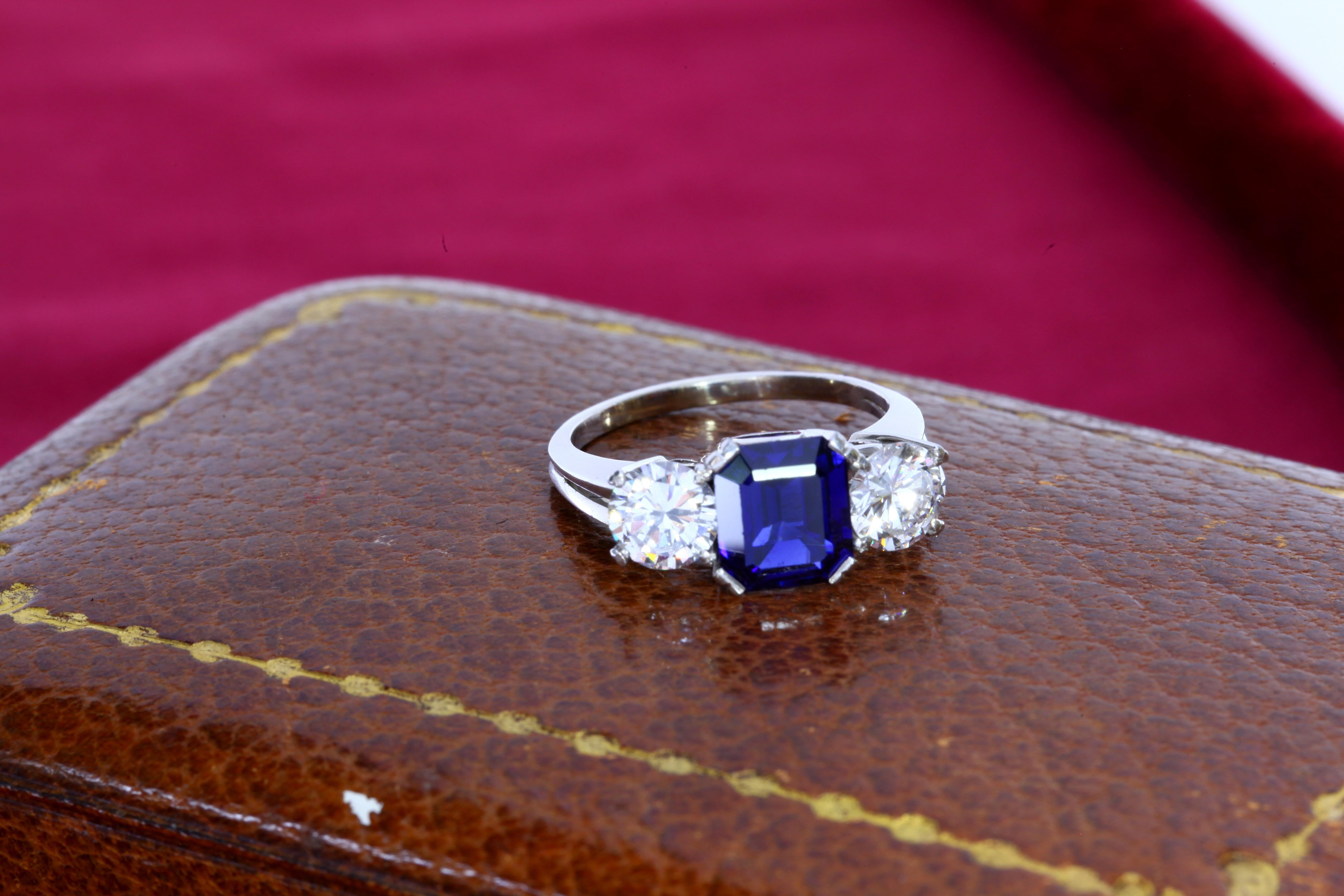 The squarish 2.22 carat octagonal step cut sapphire is flanked by two large white diamonds weighing approximately 1 carat each. The sapphire is well saturated with a deep blue color. 