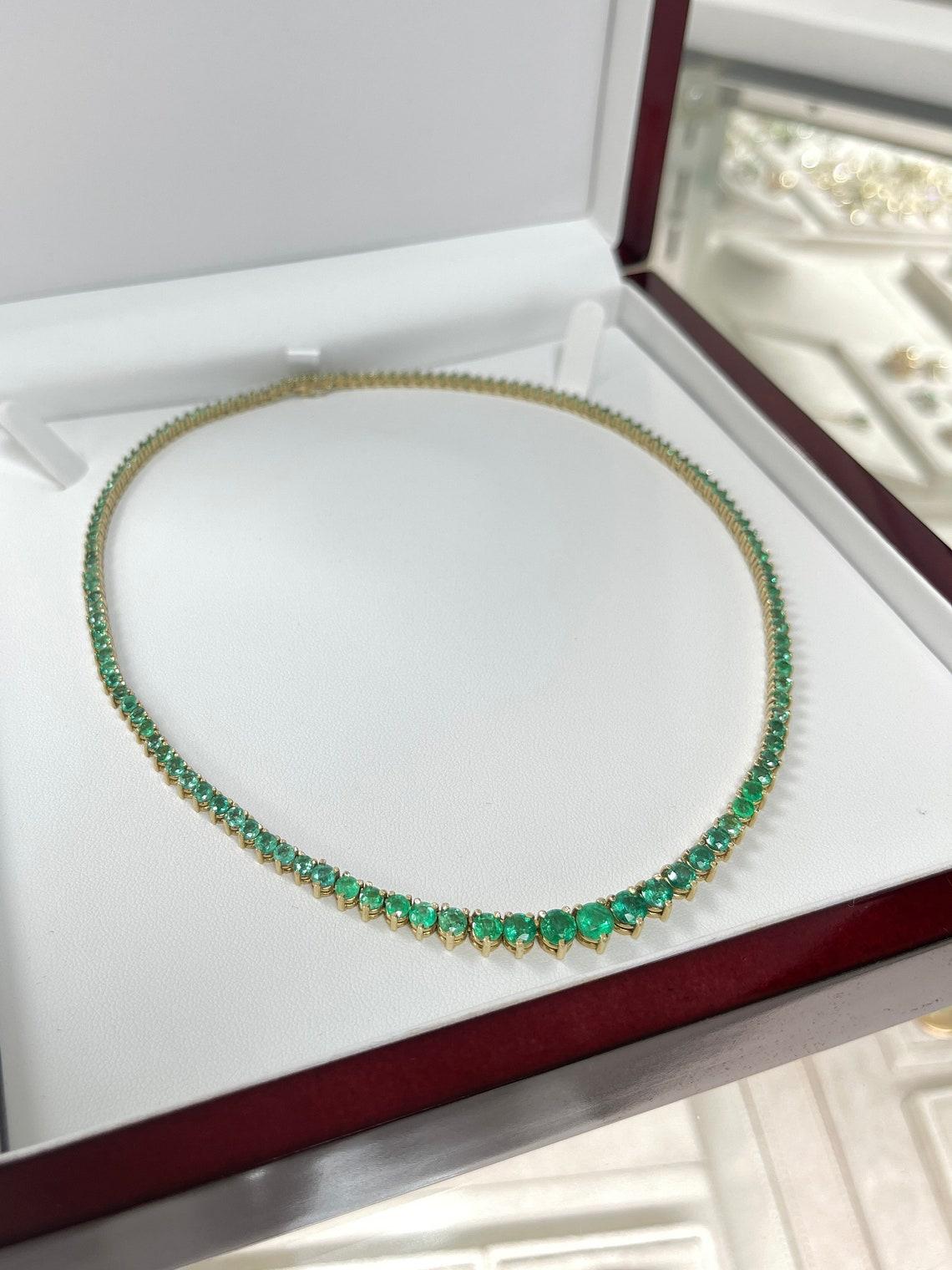 Indulge in the timeless elegance of our Emerald Tennis Necklace, a stunning piece adorned with 134 round-cut emeralds of varying sizes that seamlessly cascade around your neckline. Towards the center, the necklace boasts a captivating arrangement of