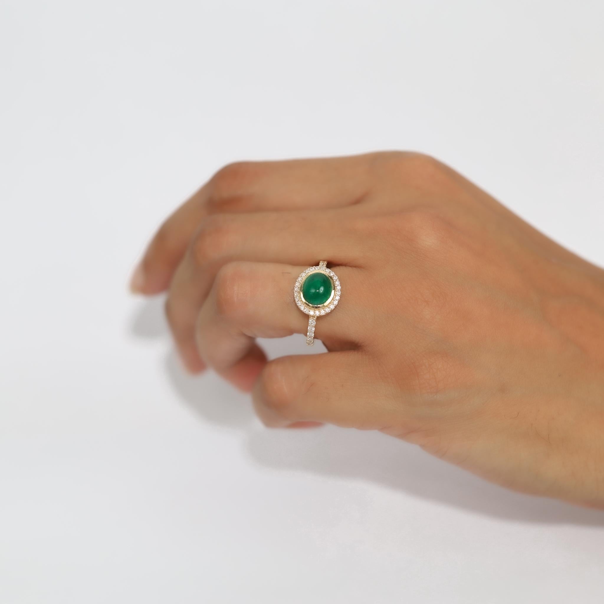 A masterpiece of refined elegance and vintage allure, this captivating halo engagement ring features a mesmerizing 2.24ct natural oval cabochon-cut emerald, cradled in the warmth of 18K yellow gold. Exuding Art Deco charm with a modern minimalist