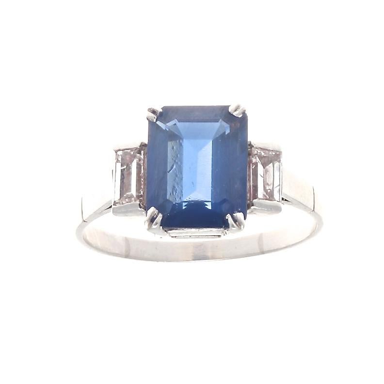 Desire and longing has revived the traditional three stone design with colorful beauty. Featuring an approximately 2.25 carat royal blue natural sapphire that is attractively accented by a single emerald cut diamond on either side. Crafted in