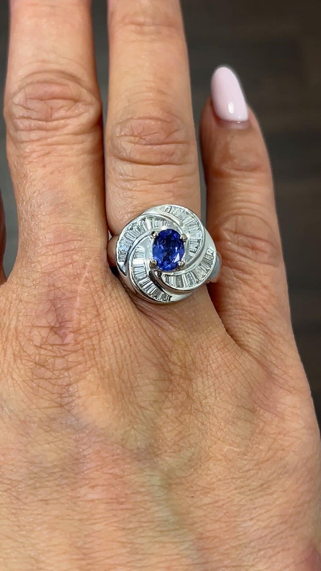 This stunning ring features a gorgeous oval-shaped tanzanite stone in a rich blue color, weighing 1.56 carats, accompanied by sparkling diamonds in a white gold setting. The ring is made of 18k gold, and has a vintage-inspired cocktail style.