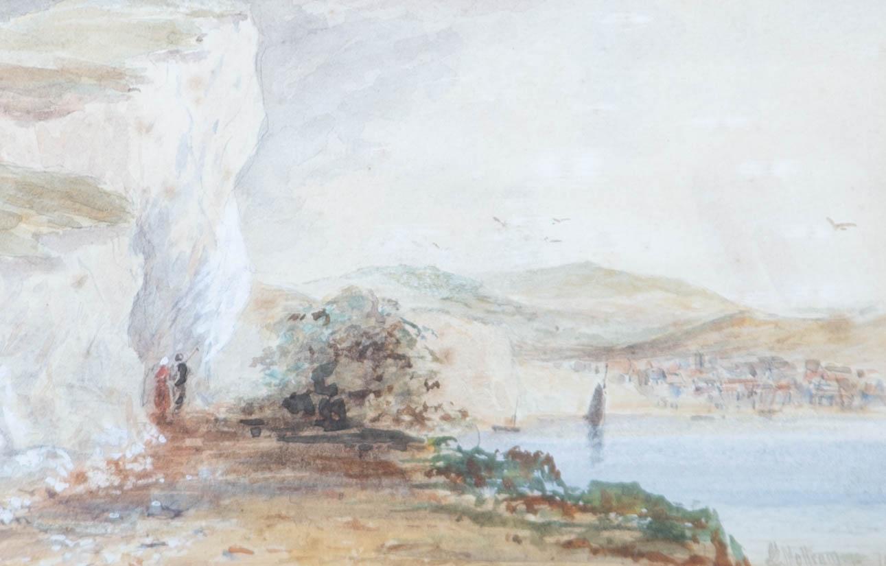 A delicate late 19th century watercolour depicting a quiet coastal scene. A small town is nestled into the hillside close to the bay and two figures walk towards the cliffside. With graphite and gouache detail. Well presented in an ornate gilt