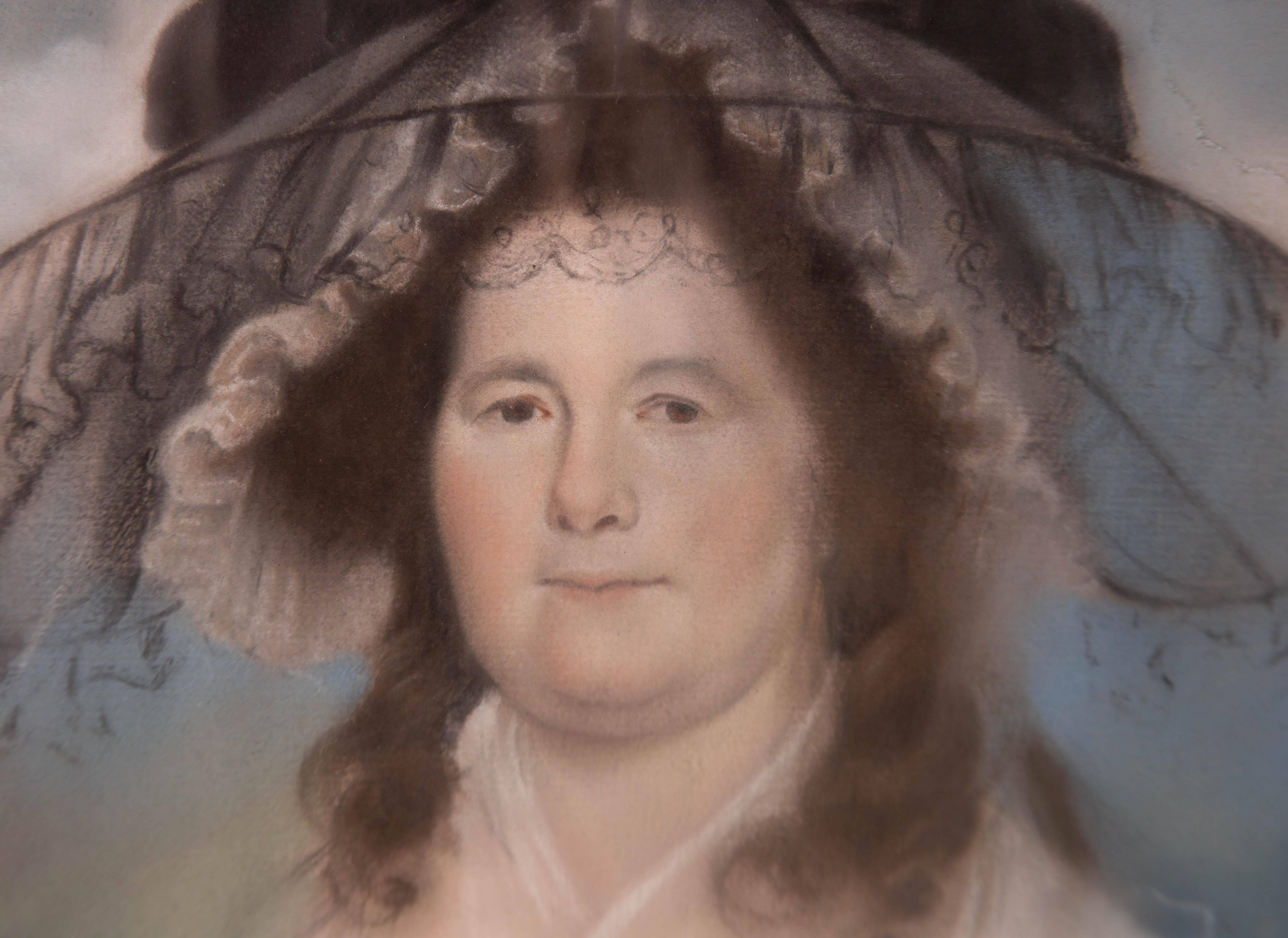 A pastel portrait of a late-eighteenth century woman wearing a substantial hat. Presented in a verre eglomise mount and a black lacquer frame with a gilt-effect inner edge. There are two labels on the verso which include information about the sitter