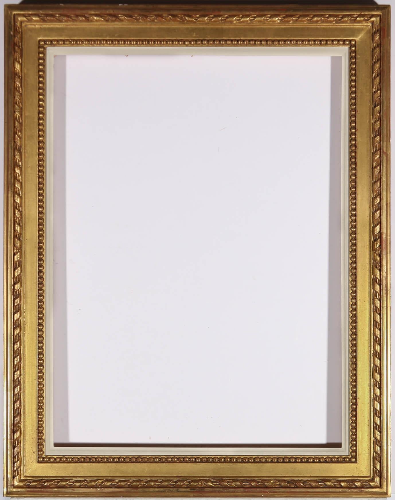 A finely carved gilt picture frame from the early 20th Century, with beaded strap work and running stick and ribbon molding, finished with a white slip. Rebate measures: 61.4cm x 45.7cm.