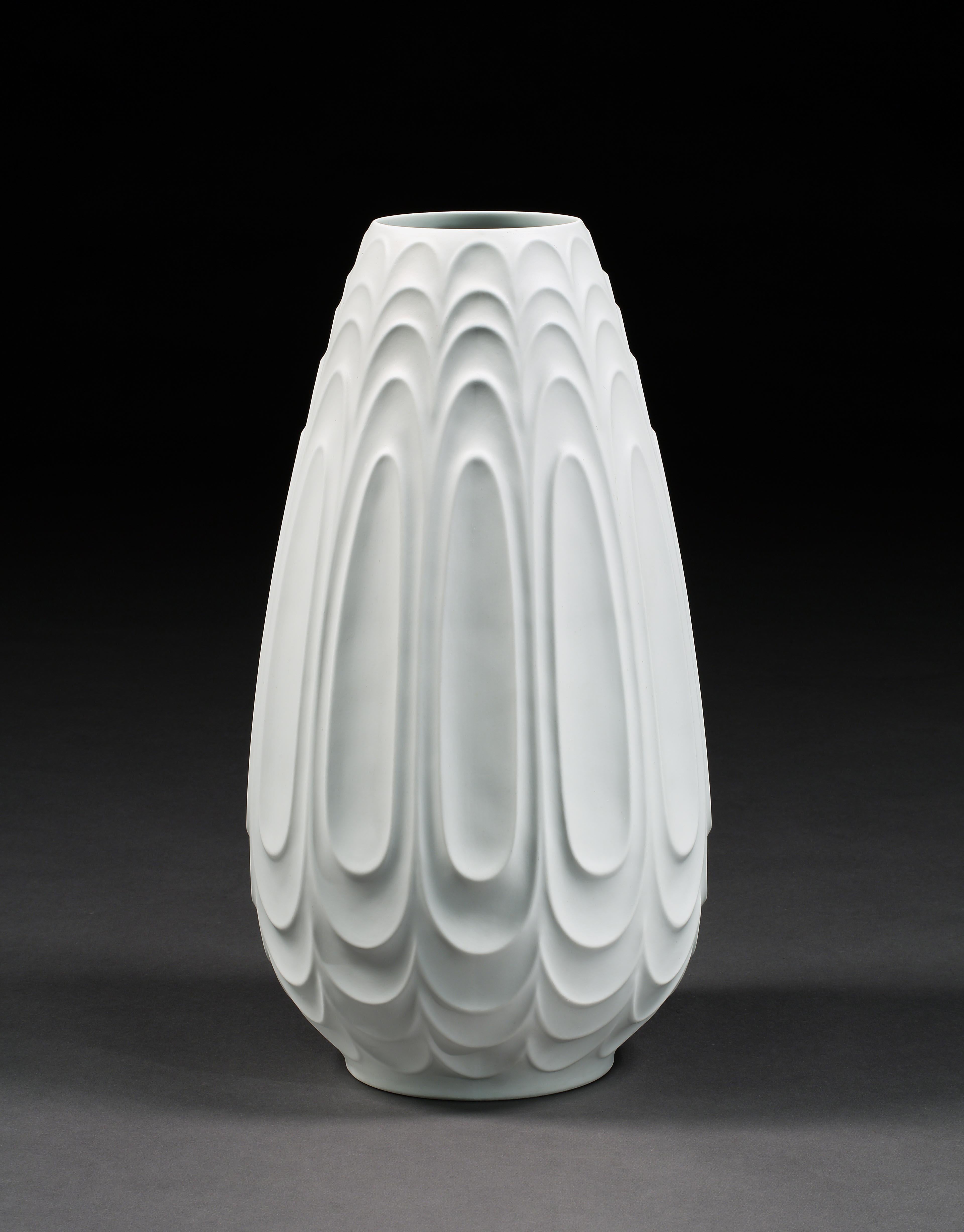 A.I.C. Heinrich, massif, blanc, porcelaine, sculpté, sur pied, vase, vers 1960. 

- La hauteur massive, le camaïeu de blanc et la surface sculptée créent une sculpture céramique rare, posée au sol, un vase. 
- Les cinq couches verticales de formes