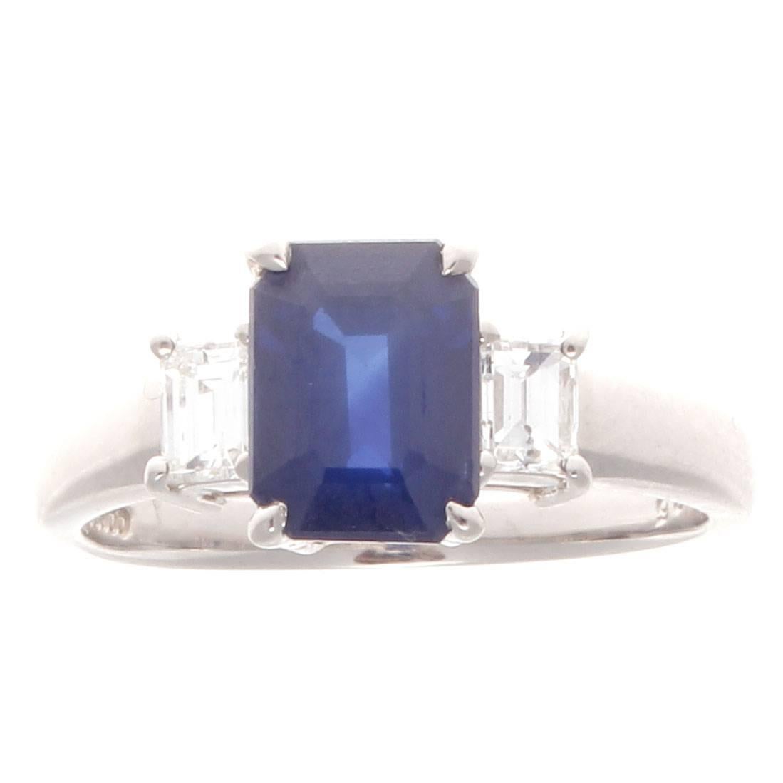 The classic and endearing three stone ring that uses a modern ideology to not conform by doing something slightly untraditional for an engagement ring. Featuring a 2.26 carat natural royal blue sapphire beautifully accented by a single emerald cut