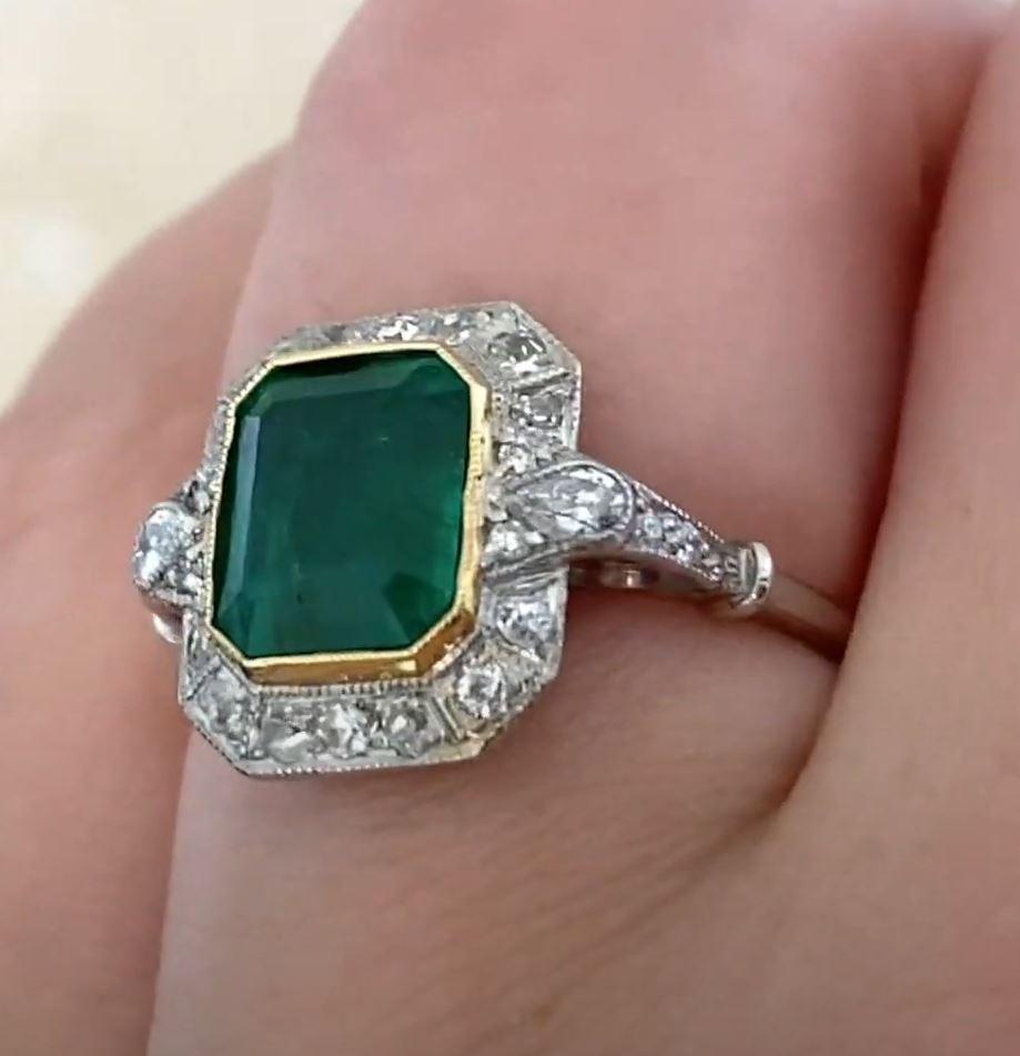 This exquisite emerald and diamond halo ring showcases a stunning approx. 2.20-carat Emerald Cut Emerald at its center, elegantly bezel-set in luxurious 18k yellow gold. The vibrant emerald is beautifully complemented by a halo of sparkling old