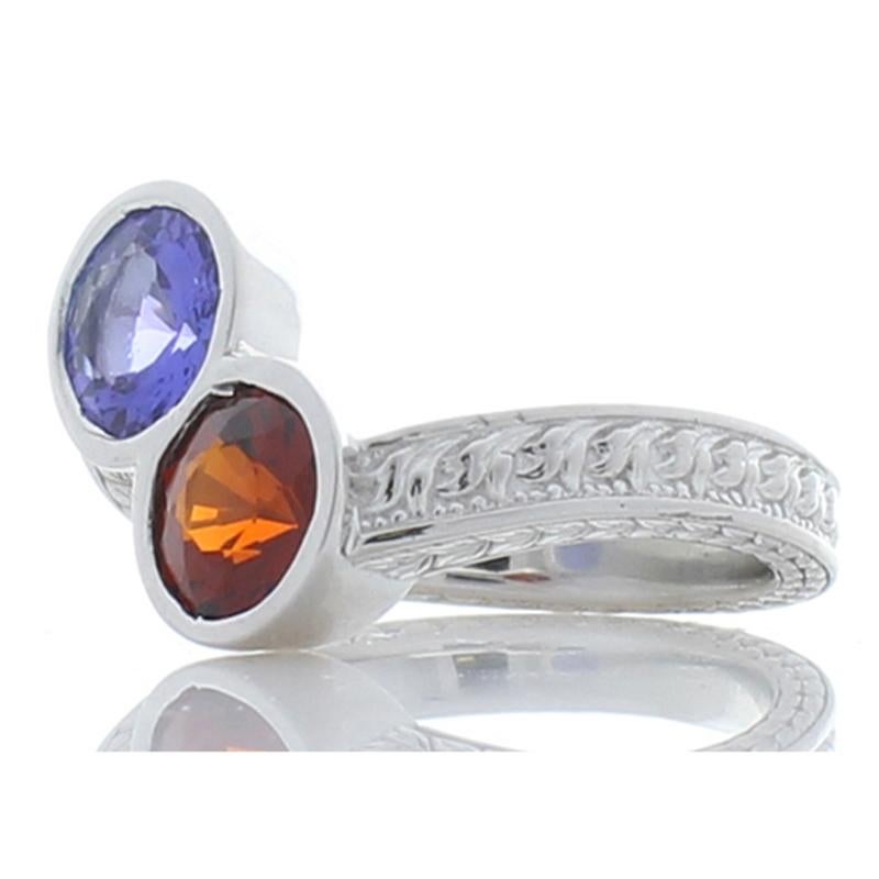 This ring features two colored gemstone centers that complement each other and your ensemble. A vivid purplish-blue - 0.99 carat tanzanite, and a deeply hued orange-red 1.28 spessartite are bezel set into an attractive bypass design. The gem sources