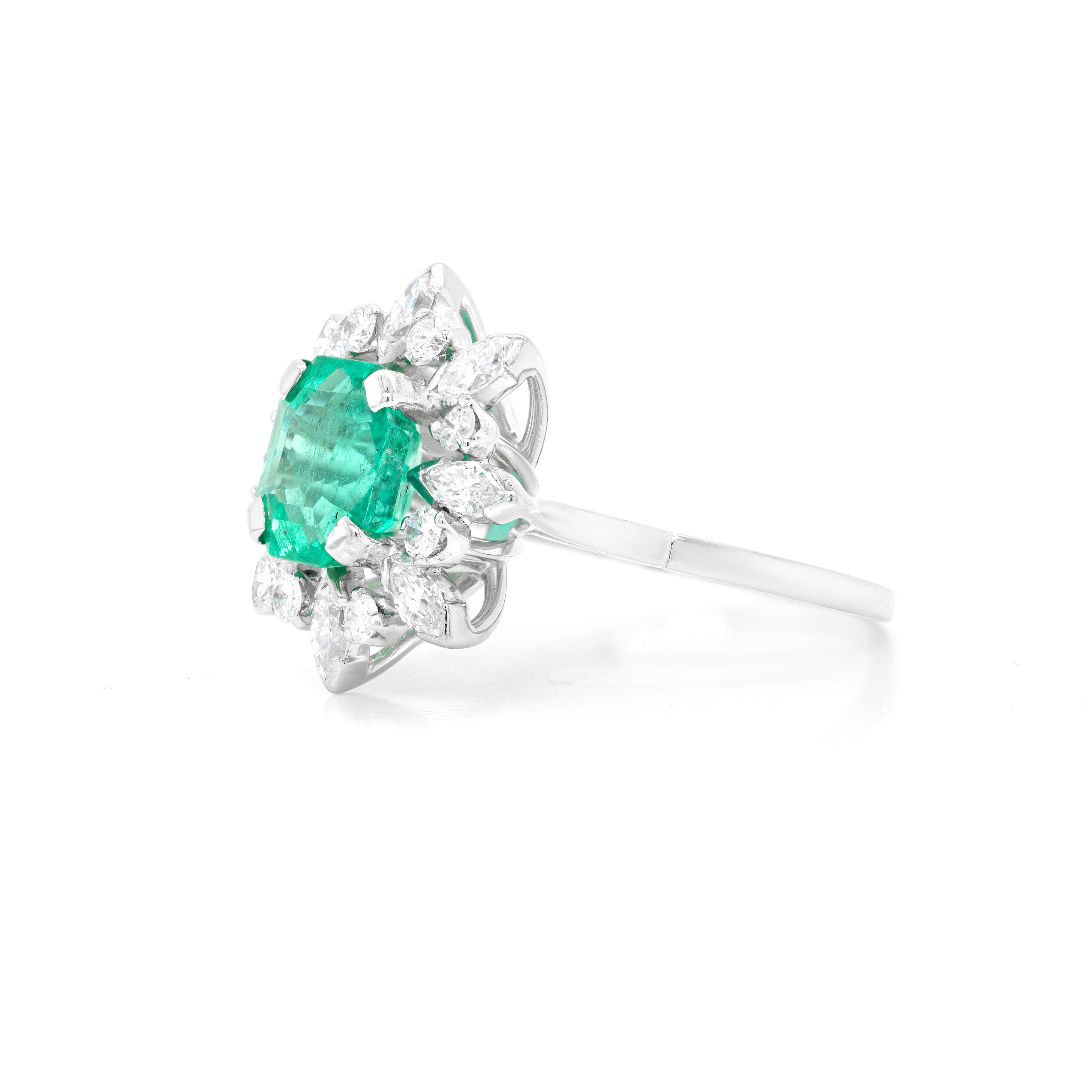 This vintage cluster engagement ring features a vibrant emerald in the centre weighing 2.27 carats mounted in a four claw, open back setting. The gemstone is perfectly surrounded by alternating marquise and brilliant cut diamonds giving a wonderful