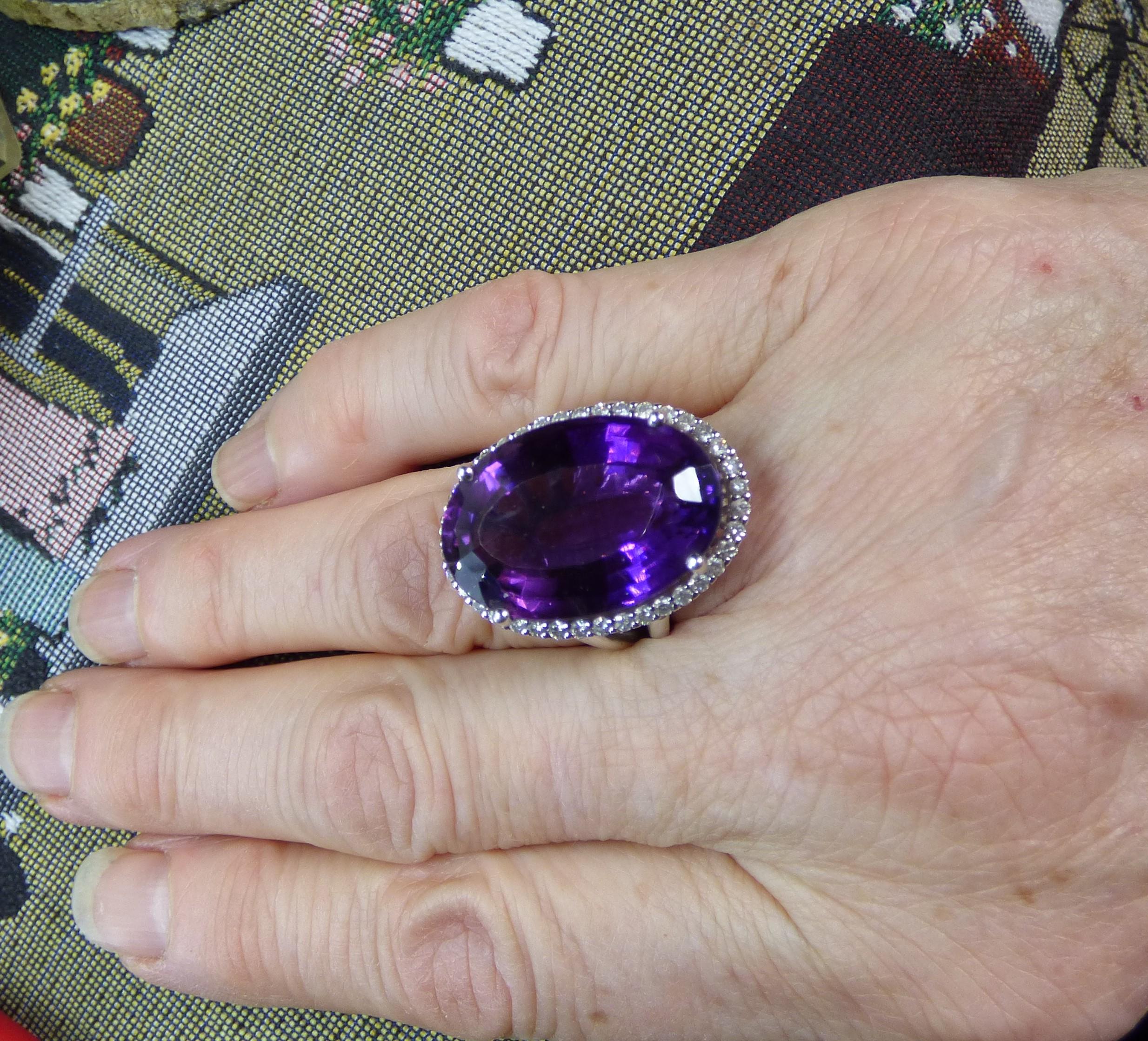 This ring stands out with a colourful natural 22ct oval cut Amethyst which measures 23X15mm.  The Amethyst is surrounded by 38 Diamonds (.65ct)  set in our own handmade 18K white gold ring with a split shank. The ring is hallmarked by the Dublin