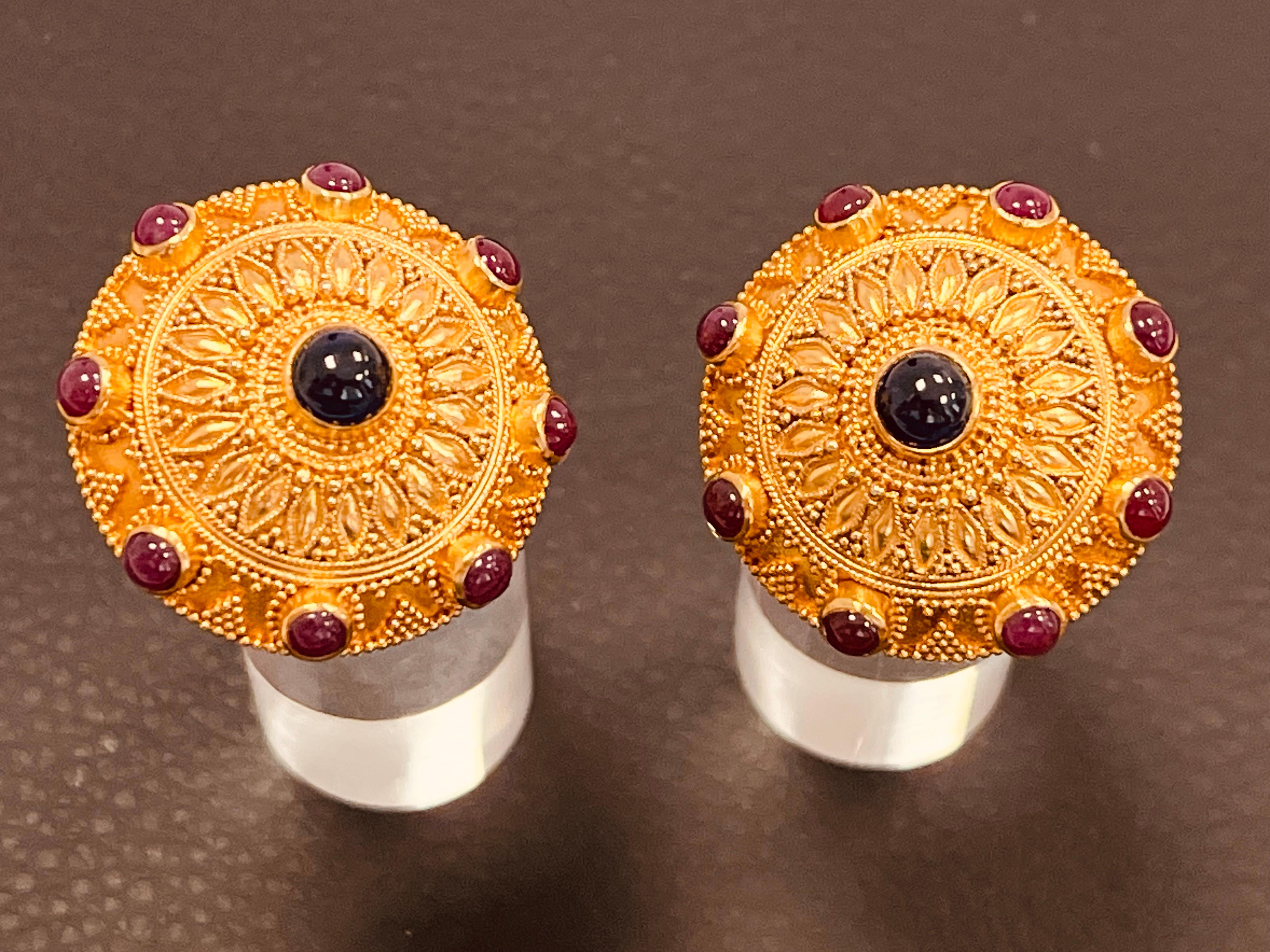 A pair of Byzantine inspired ear clips. High carat gold - between 20-22 carat. The round domed ear clip centering a cabochon sapphire and cabochon ruby border. The whole decorated with filigree and granulation work. The back lightly hammered with