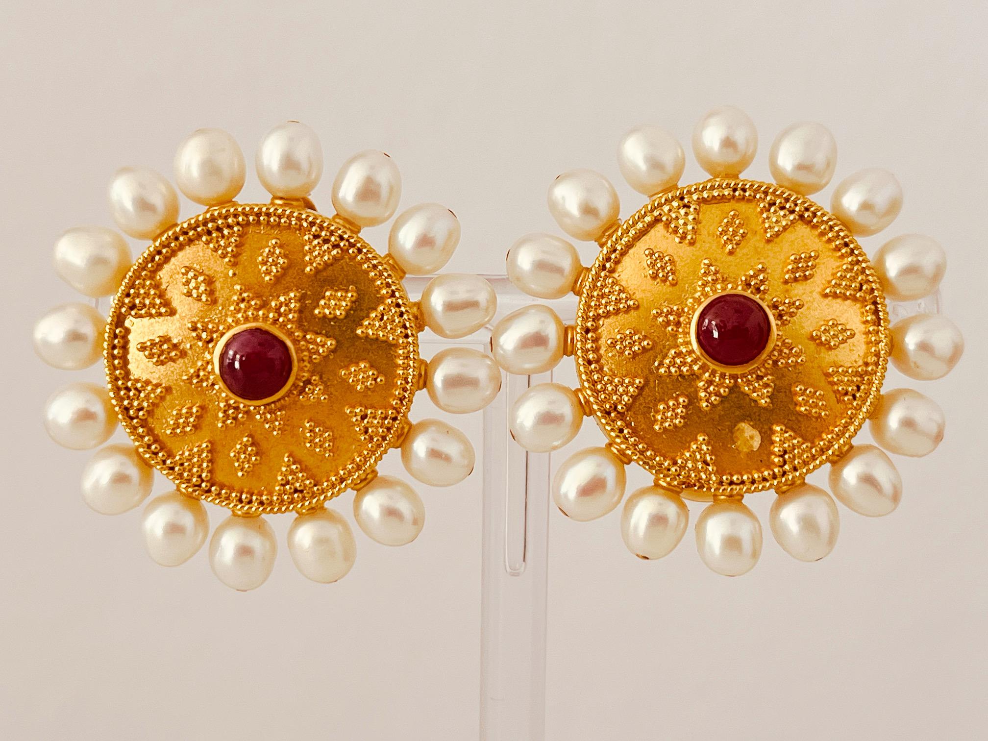 A pair of 22ct yellow gold, granulated disc earrings, centrally set with a cabochon ruby and surrounded by freshwater cultured pearls. Circa 1990. Diameter 3.3cm. 25.4 grams. Both earrings with maker's marks and signed 