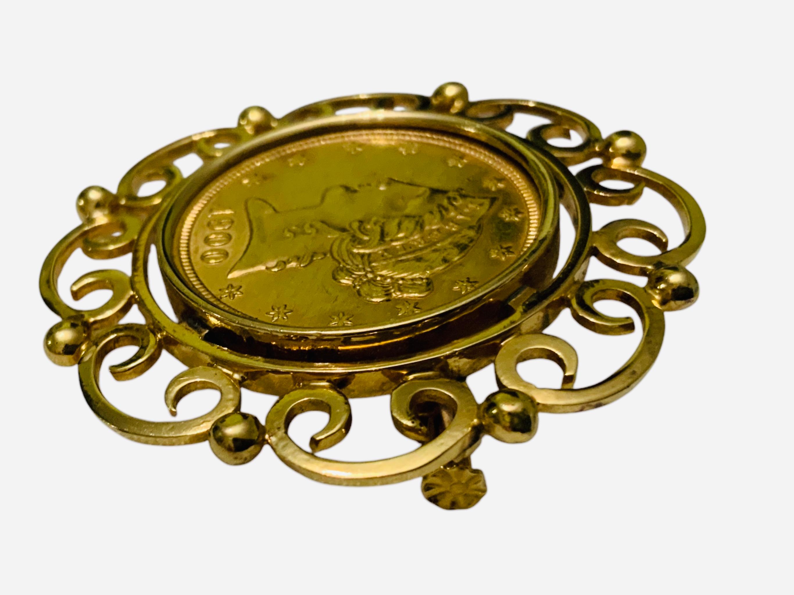 This is a 22K Gold Coin Brooch. It depicts a circa 1900 United States of America yellow gold coin mounted and adorned with an 18K gold frame made of a garland of C- scrolls. One side portrays the Liberty  profile 1900 and the other one, the USA