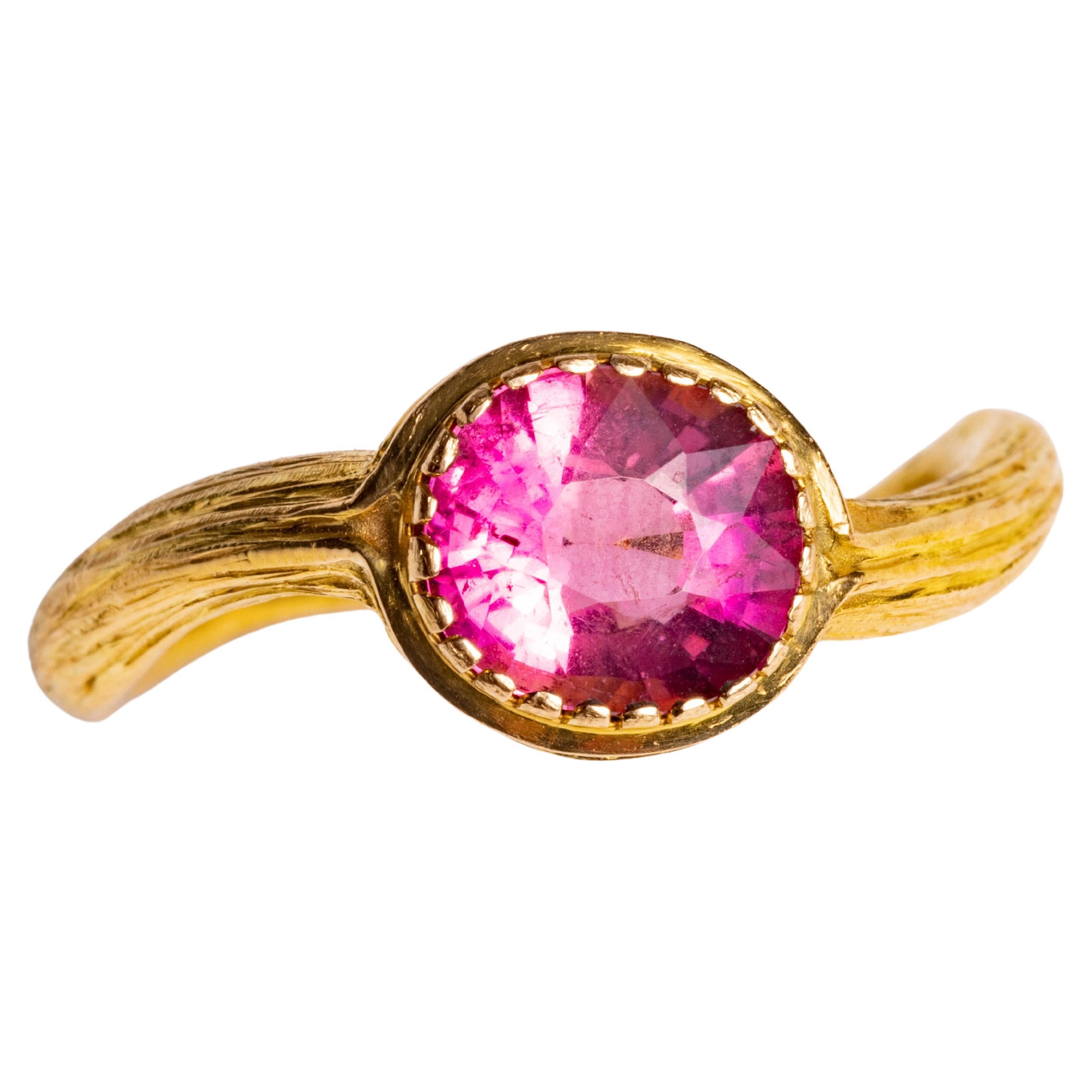 A 22K gold ring with textured tooling featuring a round, brilliant cut pink tourmaline in a bezel setting.  Gold band has a subtle serpentine shape to it.

The fine jewelry collection is sourced, designed or created by Deborah Lockhart Phillips.