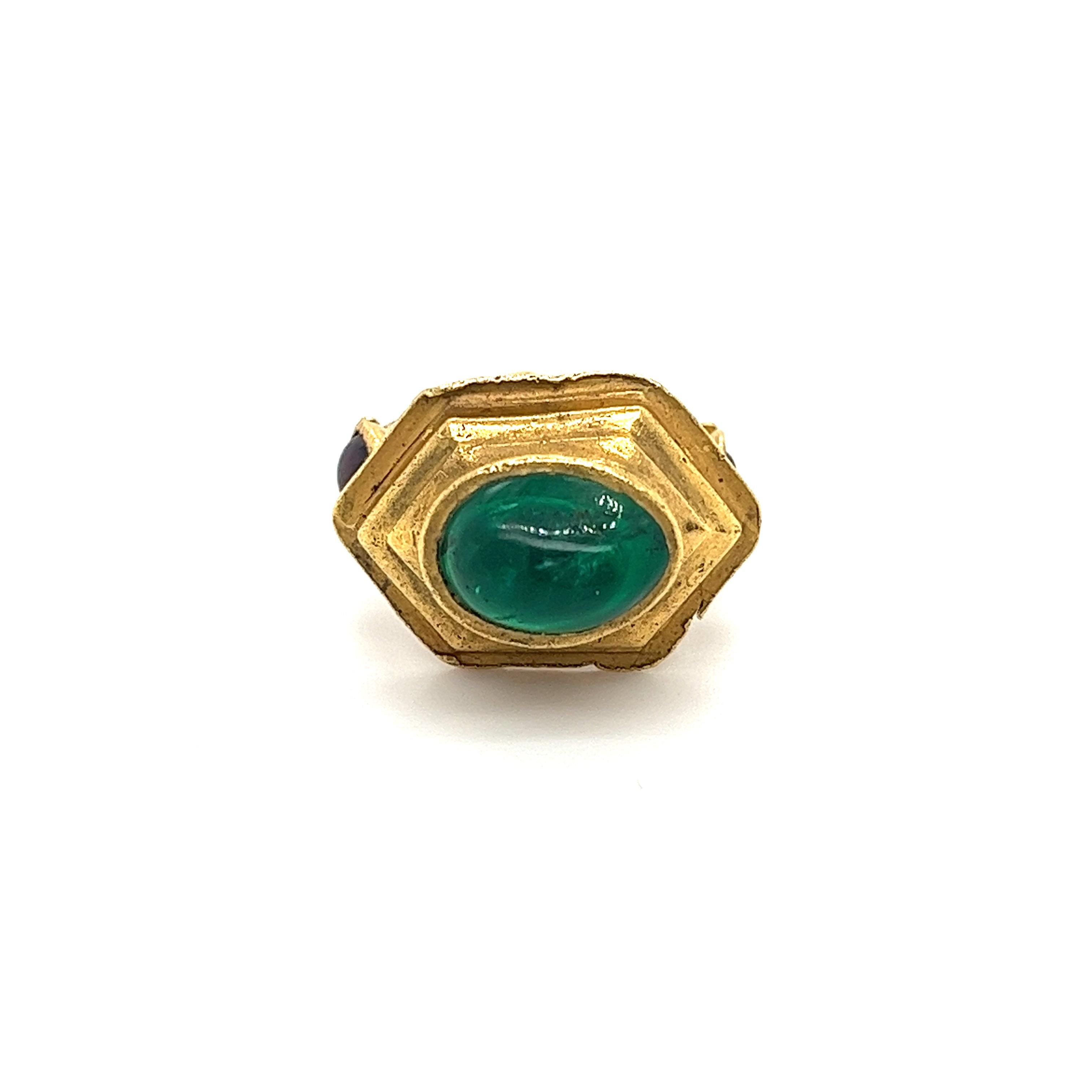 This Egyptian revival ring mounts a 3-carat cabochon cut natural emerald, set in 22 karat solid gold. Featuring 2 cabochon cut garnet gemstones along the ring shank. The emerald displays a rich, vibrant natural green color. This piece is handmade