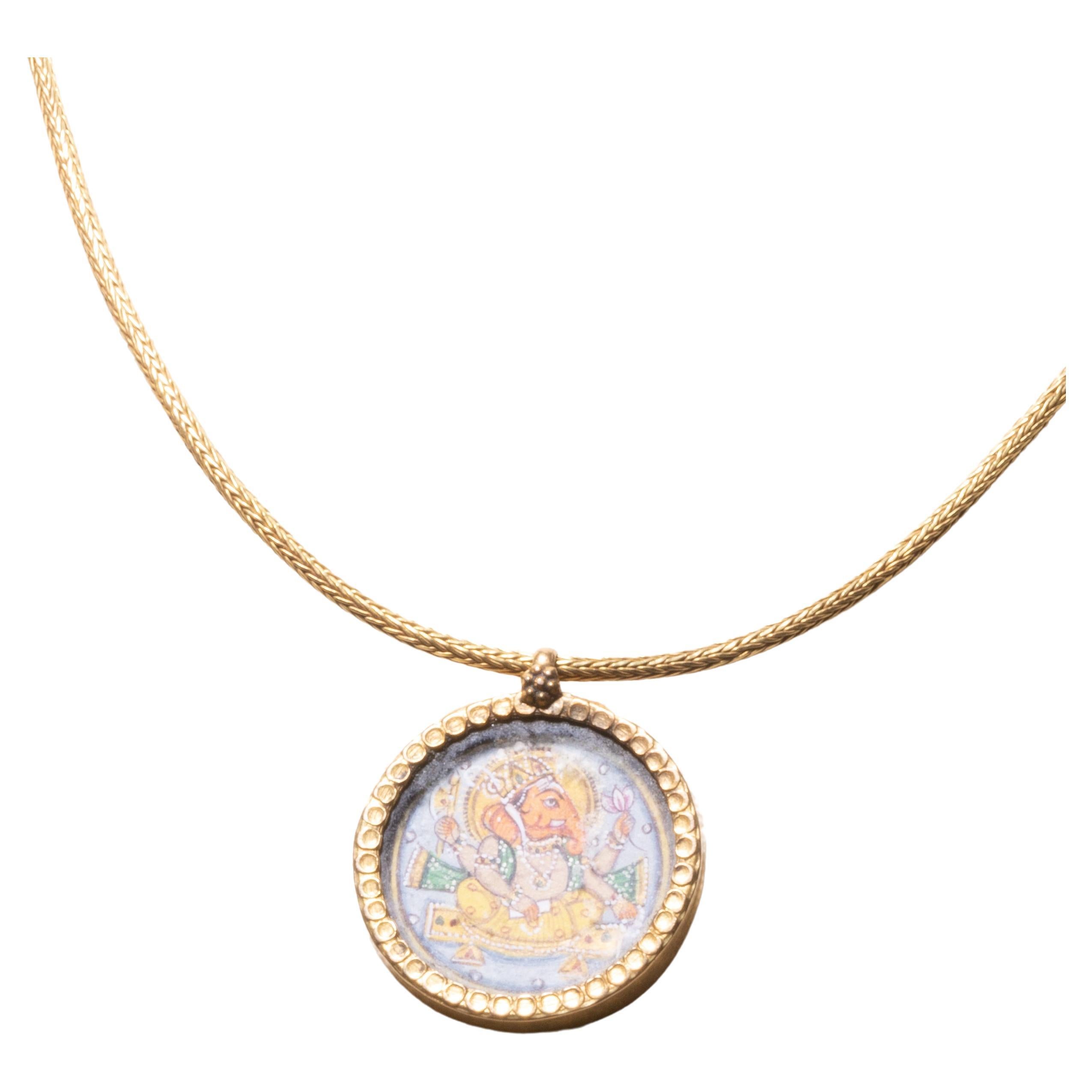 A charming and auspicious pendant necklace featuring a finely detailed, hand-painted Ganesh (the Hindu deity known as is the remover of obstacles).  It is encased in 22K gold with a gold backing and tooled workmanship around the border.  The chain
