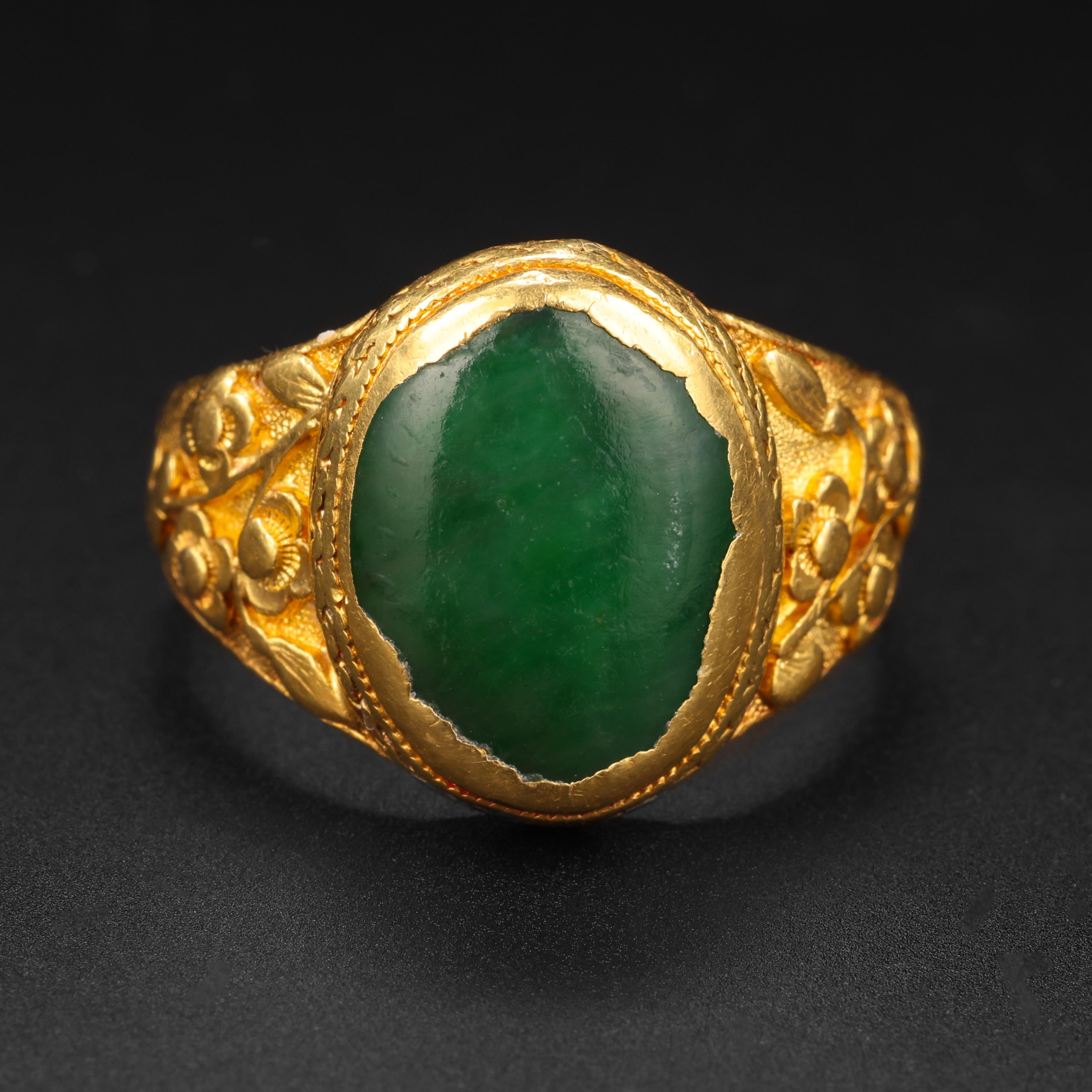 This impossibly rich 22K yellow gold and jade ring was created by hand near the end of the 19th century in China. Featuring deeply carved shoulders depicting highly detailed flowers; the recessed background has a stippled appearance. The