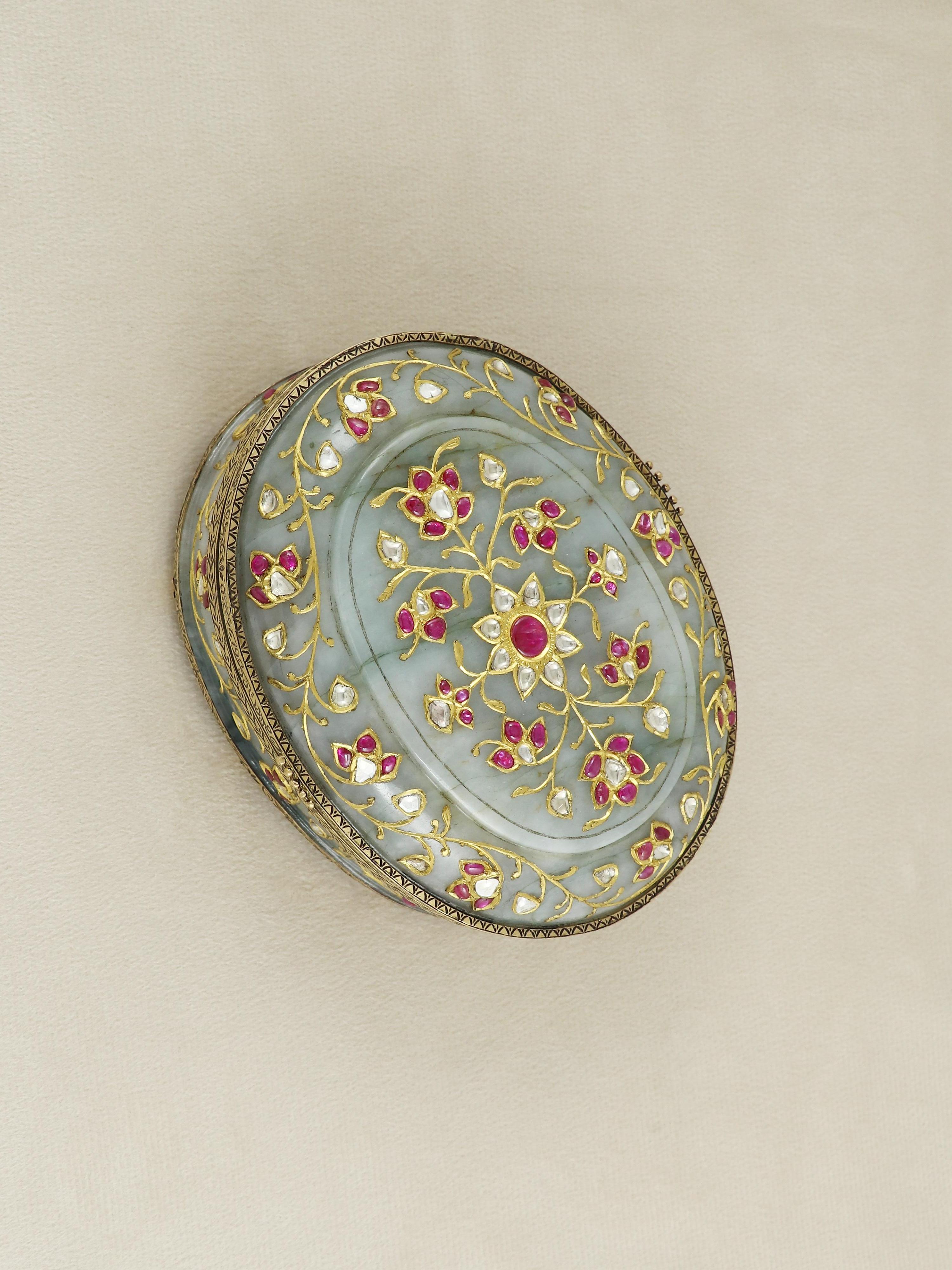 A striking union of regal artistry and masterful gemcraft, this exquisite oval box is meticulously carved from fine jadeite jade and adorned with 22K solid gold detailing. The body of the box, fashioned from a single piece of lustrous green jadeite,