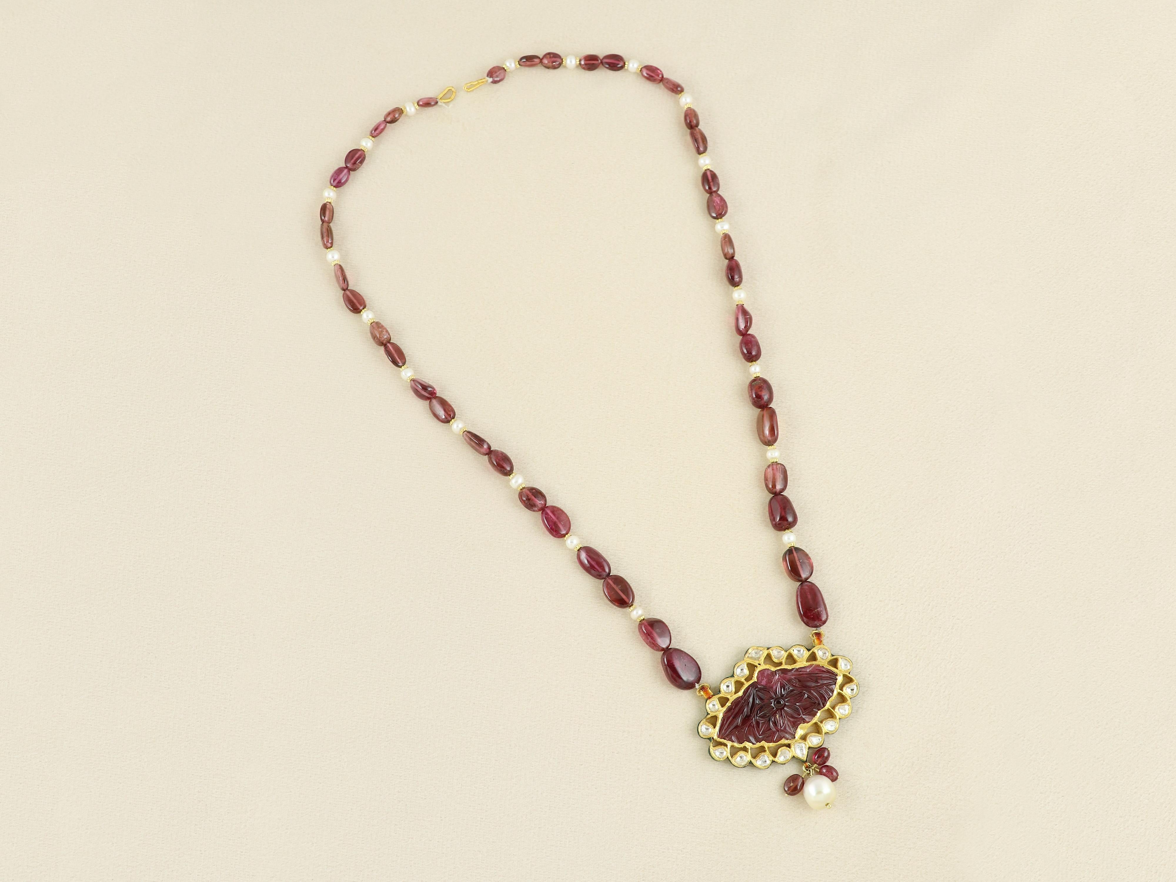 An embodiment of regal elegance and spiritual symbolism, this one-of-a-kind pendant is handcrafted in pure 22K gold and centered around a natural carved tourmaline. The gemstone is intricately engraved with a Mughal floral motif—reminiscent of the