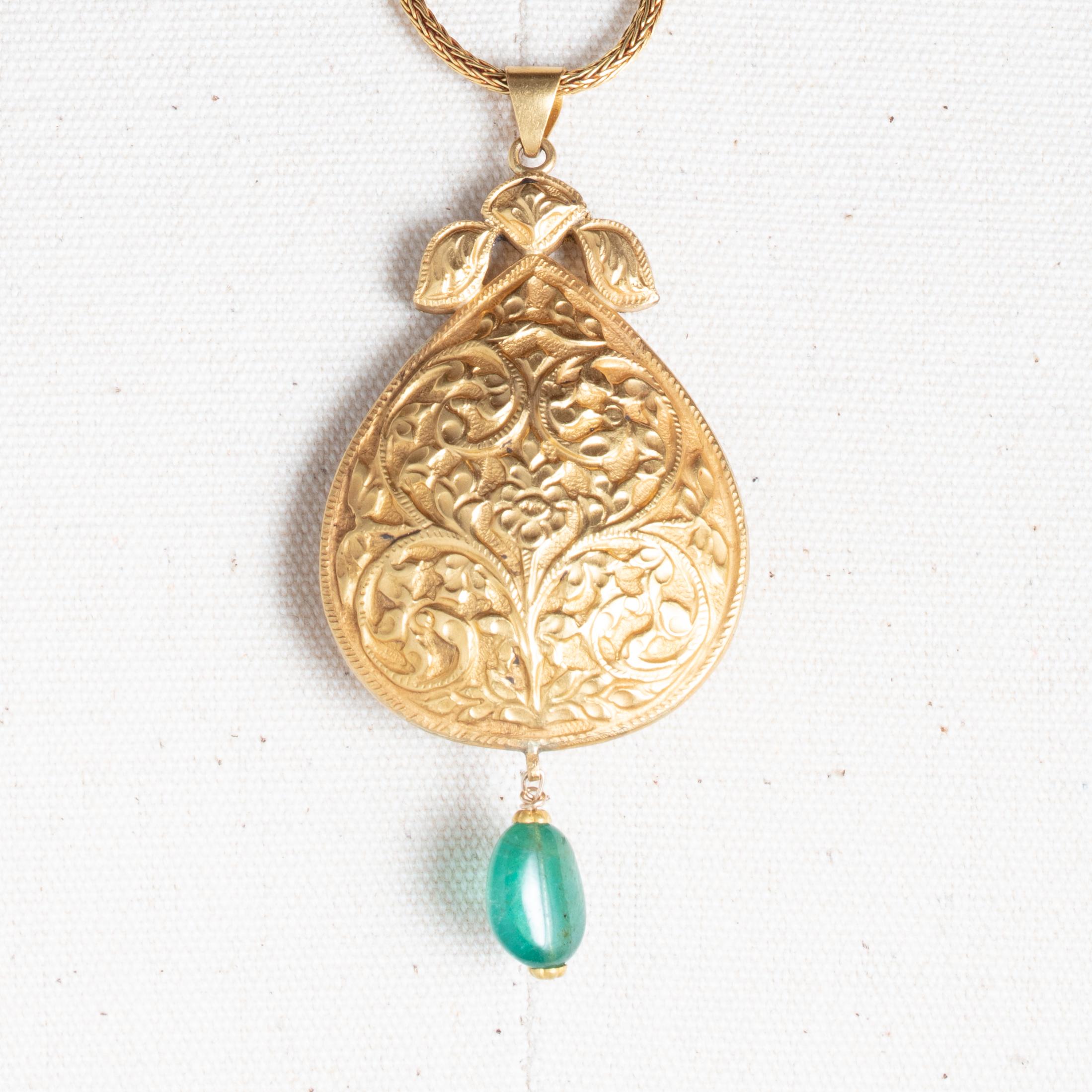 A lovely 22K gold Nava Ratna pendant comprised of precious and semi-precious stones.  Fine tooling on the border and reversible to a repousse` floral and vine motif on the other side.  The length of the pendant is 2.5 inches and a tumbled emerald