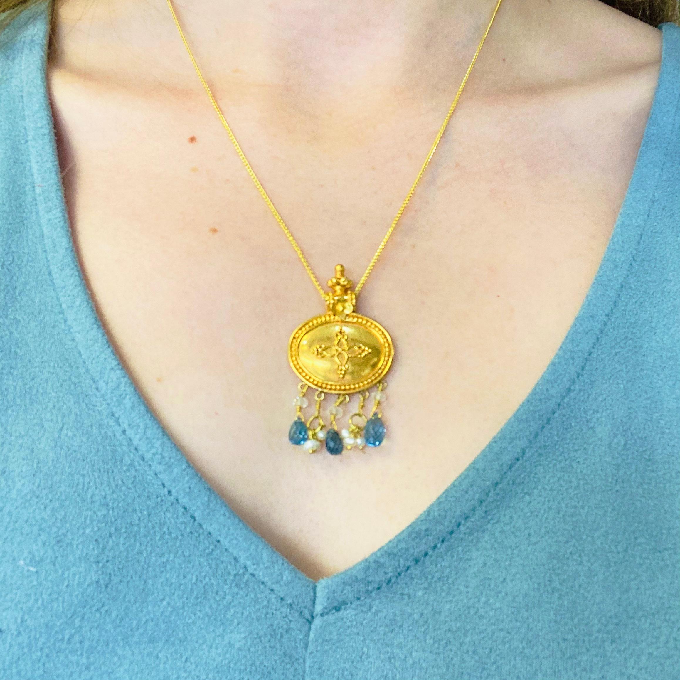 This exquisite 22k yellow gold pendant is truly one of a kind! Adorned with delicate dangling blue topaz briolettes, seed pearls, and clear quartz, this elegant eye-catching pendant will move gracefully with its wearer throughout the day. It comes