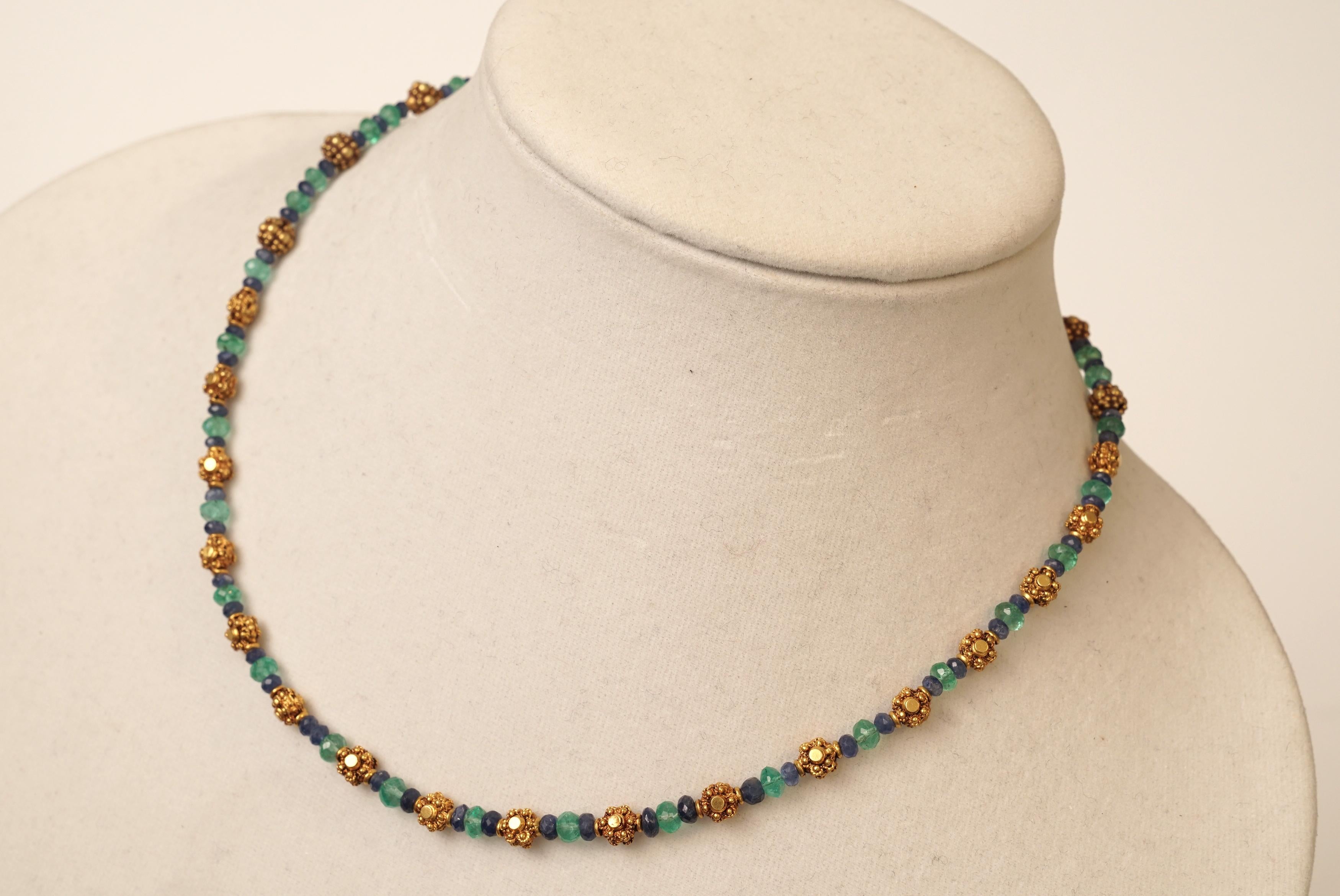 Una delicata ma significativa collana in oro 22K con zaffiri blu sfaccettati e smeraldi colombiani sfaccettati.  Le perle d'oro hanno un motivo floreale e presentano un peso significativo dell'oro e una fine granulazione.  Chiusura con gancio a S e