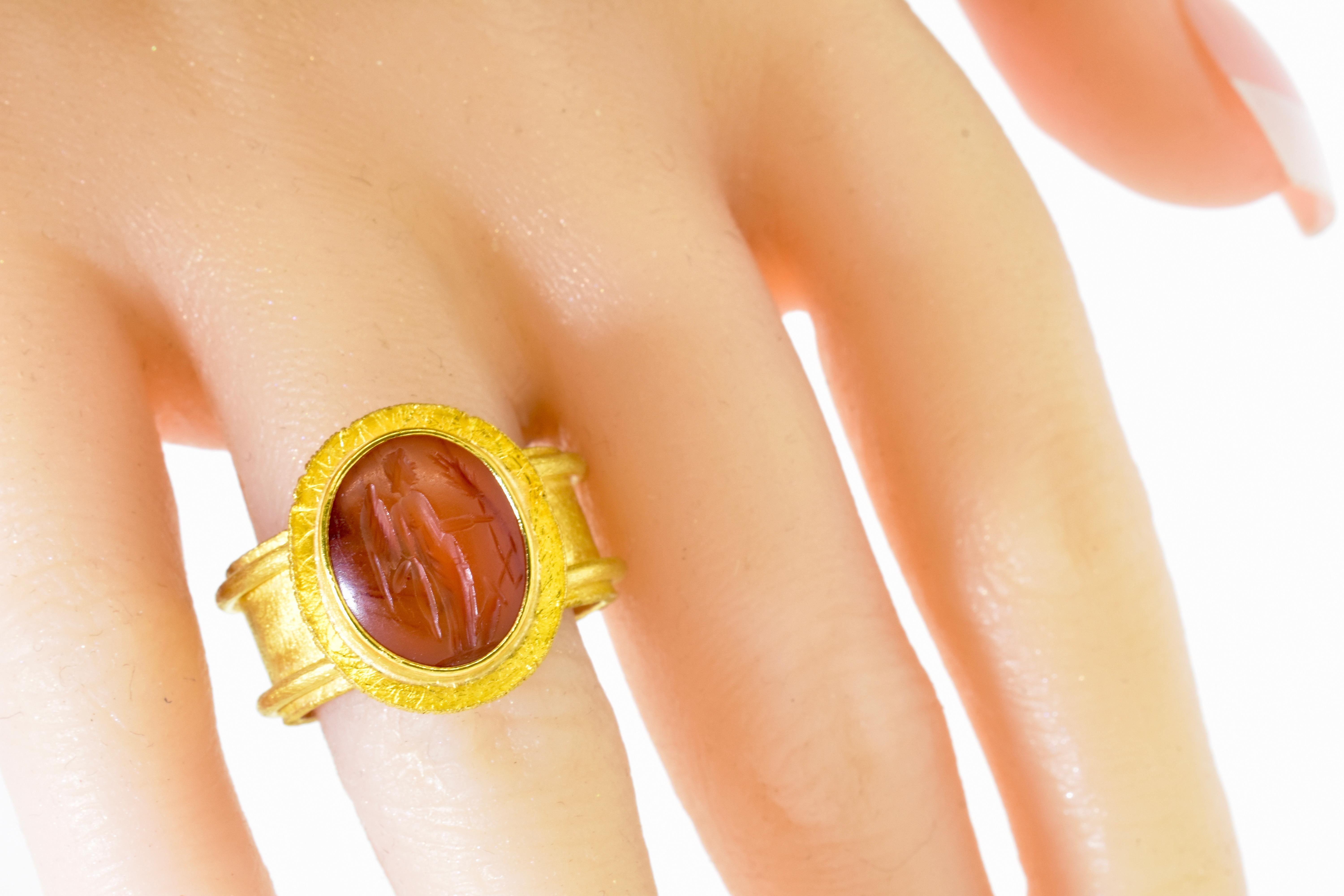 22K gold contemporary ring centering an antique carnelian intaglio of a standing angel extending an olive branch - signifying peace. The intaglio measures 14.4 mm by 11.5 mm. The wide band measures 10.1 mm.  This ring is signed by the jewelry
