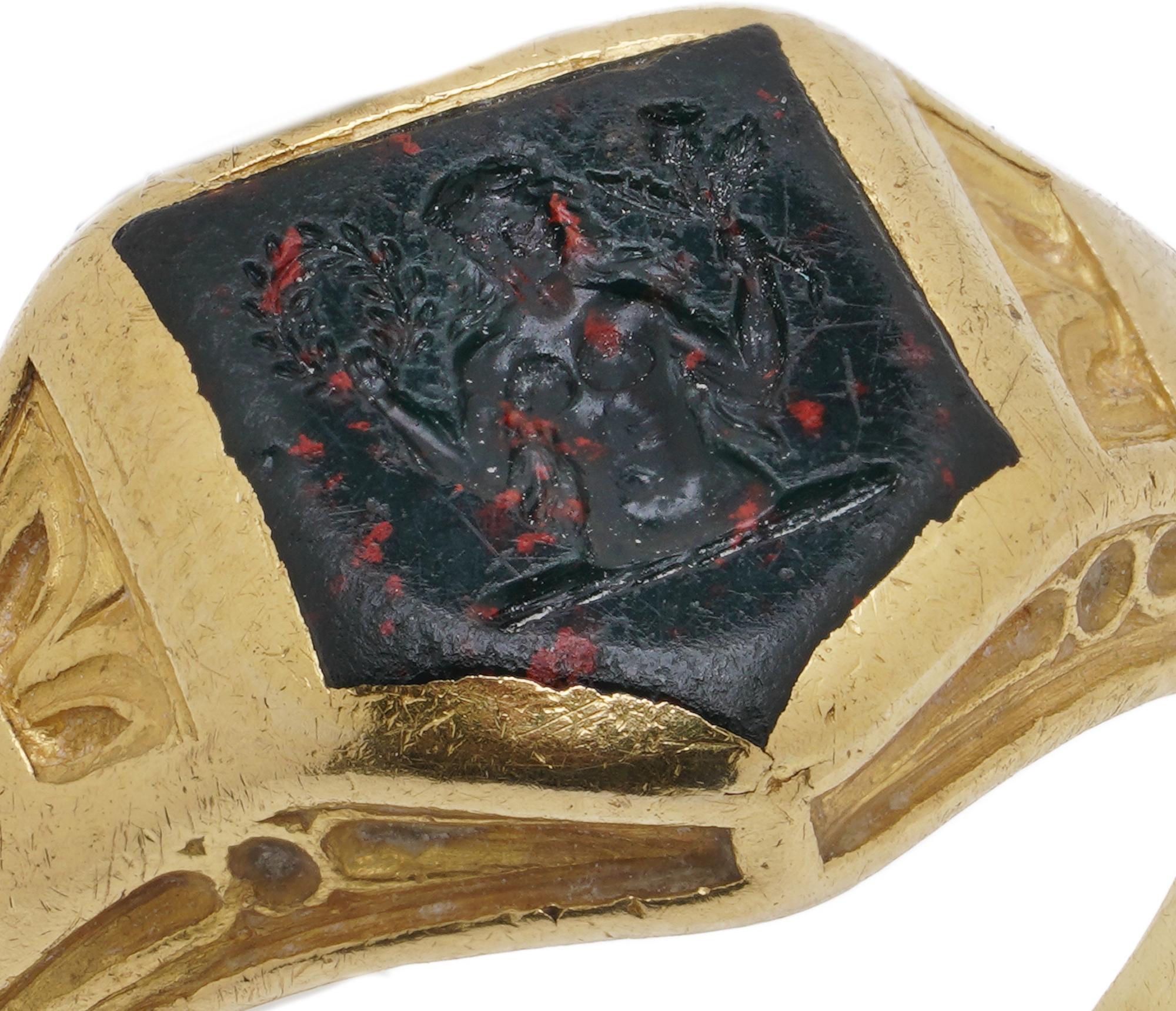 Dieser antike Siegelring zeigt ein Blutstein-Intaglio, das in eine Fassung aus 22-karätigem Gelbgold gefasst ist. Die Intaglio zeigt Demeter (griechisch: Δημήτηρ), die griechische Göttin der Ernte, des Ackerbaus und der Fruchtbarkeit. Sie ist oft
