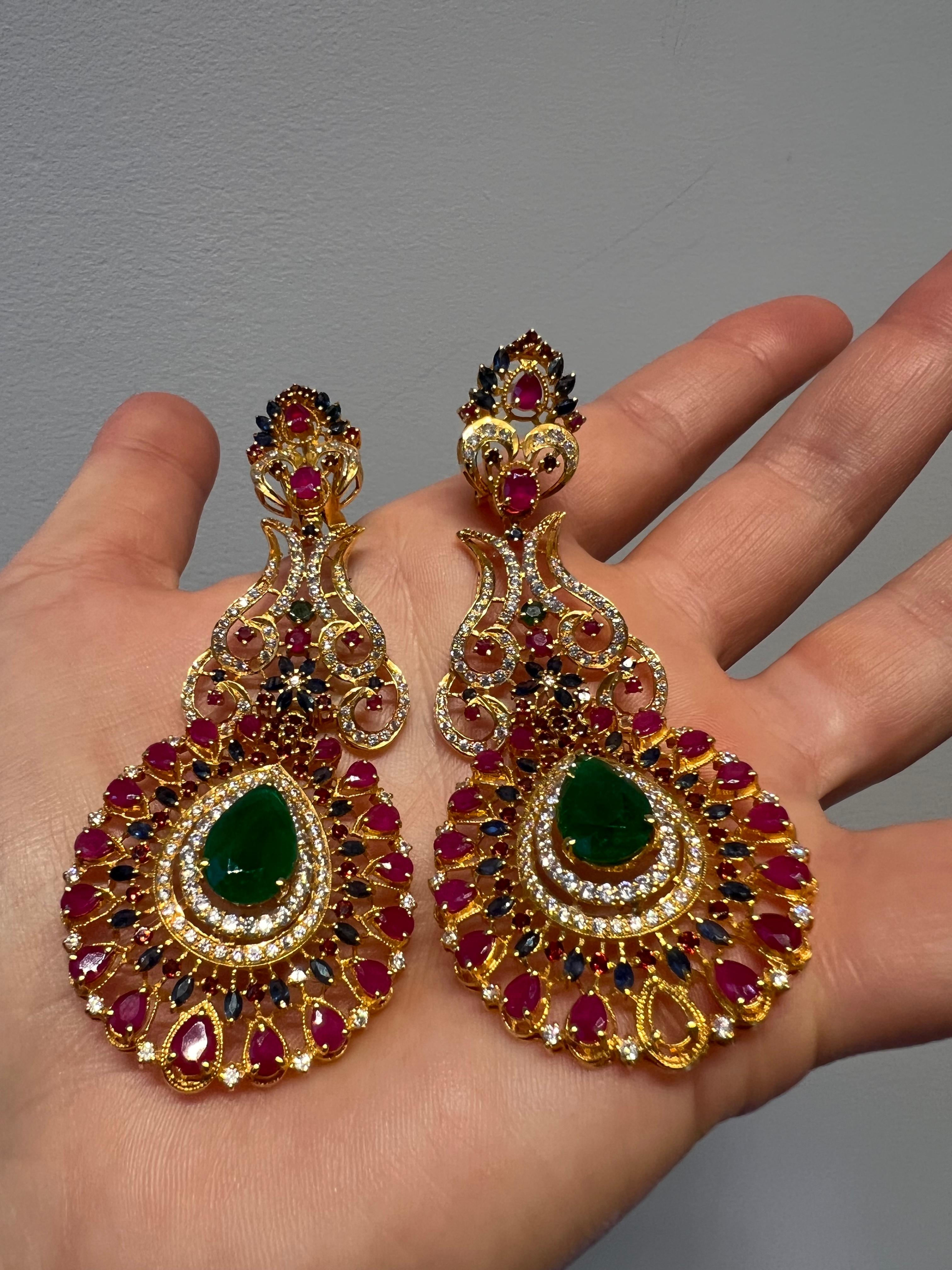 Discover the opulent charm of these 22k Gold Earrings adorned with an exquisite array of diamonds, rubies, emeralds, and sapphires. With approximately 2 carats of sparkling round diamonds, 8 carats of vibrant emeralds, 3 carats of rich rubies, and