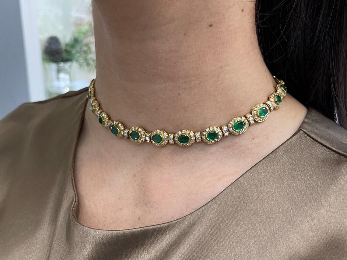 Erhöhen Sie Ihre Eleganz mit unserer exquisiten Choker-Halskette mit Smaragden und Diamanten. Dieses königliche Meisterwerk besteht aus 26 Smaragden im Ovalschliff, von denen jeder eine lebhafte, satt smaragdgrüne Farbe, einen dunklen Ton und einen