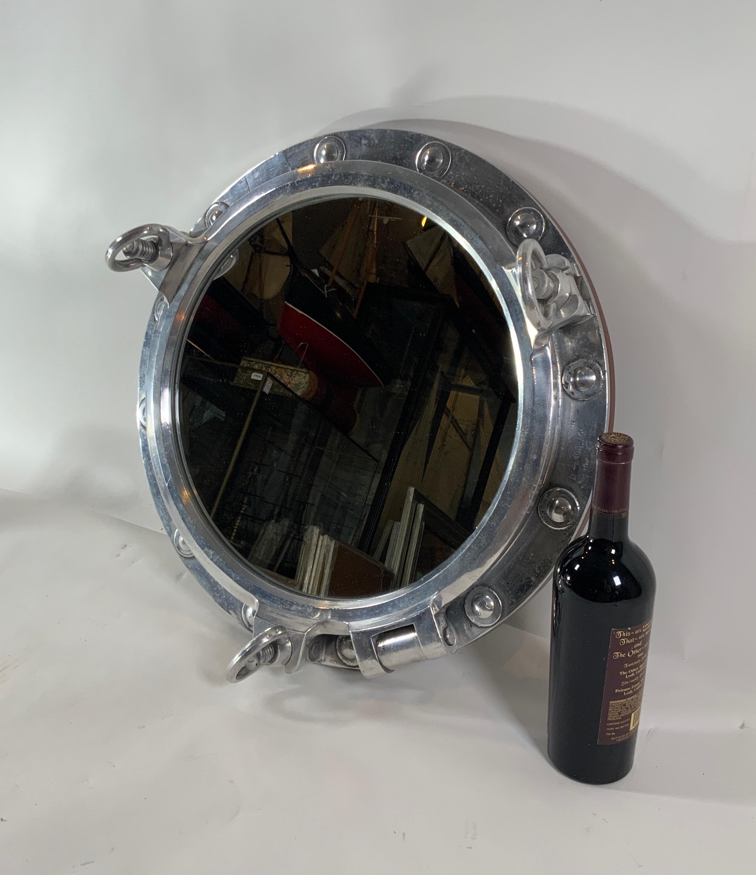 Massive authentic polished aluminum ship's porthole fitted with a glass mirror. Door is hinged and fitted with three dogbolts. This is a large impressive size and scale. The highly polished porthole is also fitted with a teakwood trim ring on the