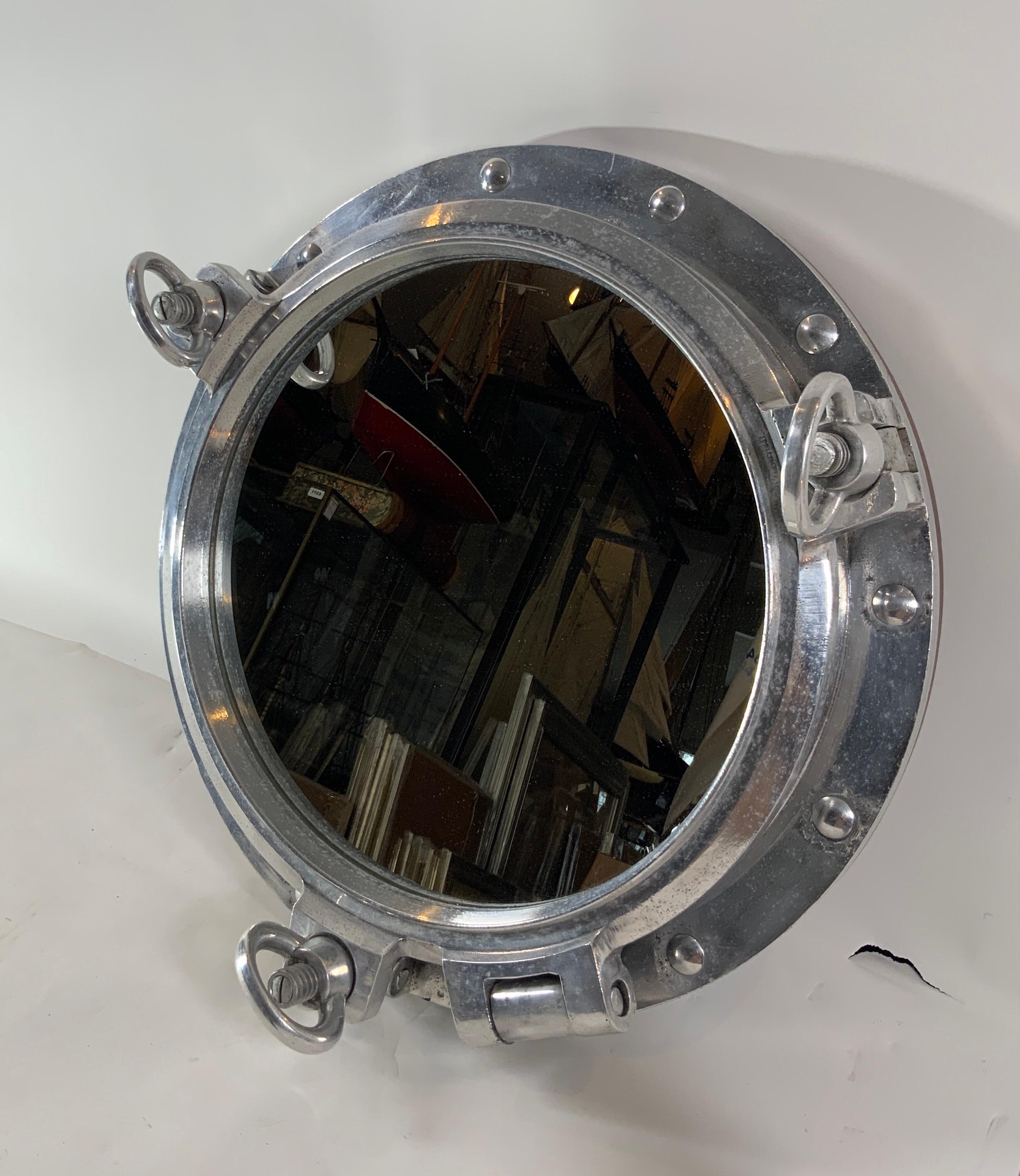 Massive authentic polished aluminum ship's porthole fitted with a glass mirror. Door is hinged and fitted with three dogbolts. This is a large impressive size and scale. The highly polished porthole is also fitted with a teakwood trim ring on the